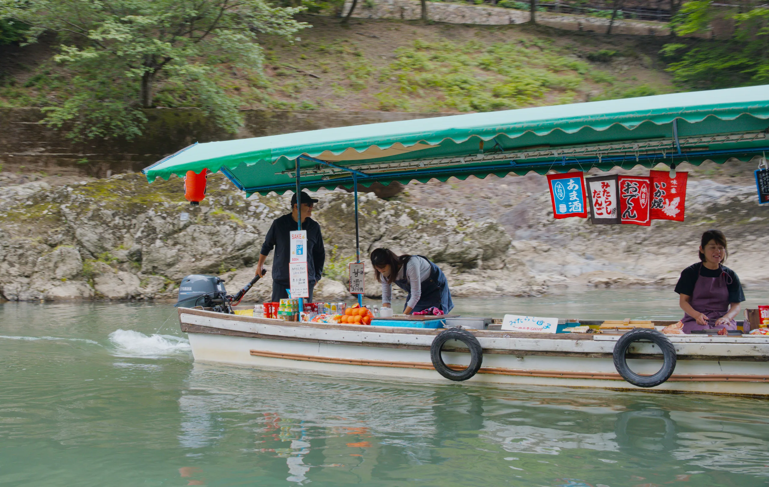 Riverboats sheltered by a turquoise canopy hold stacked supplies and vendors along the water.