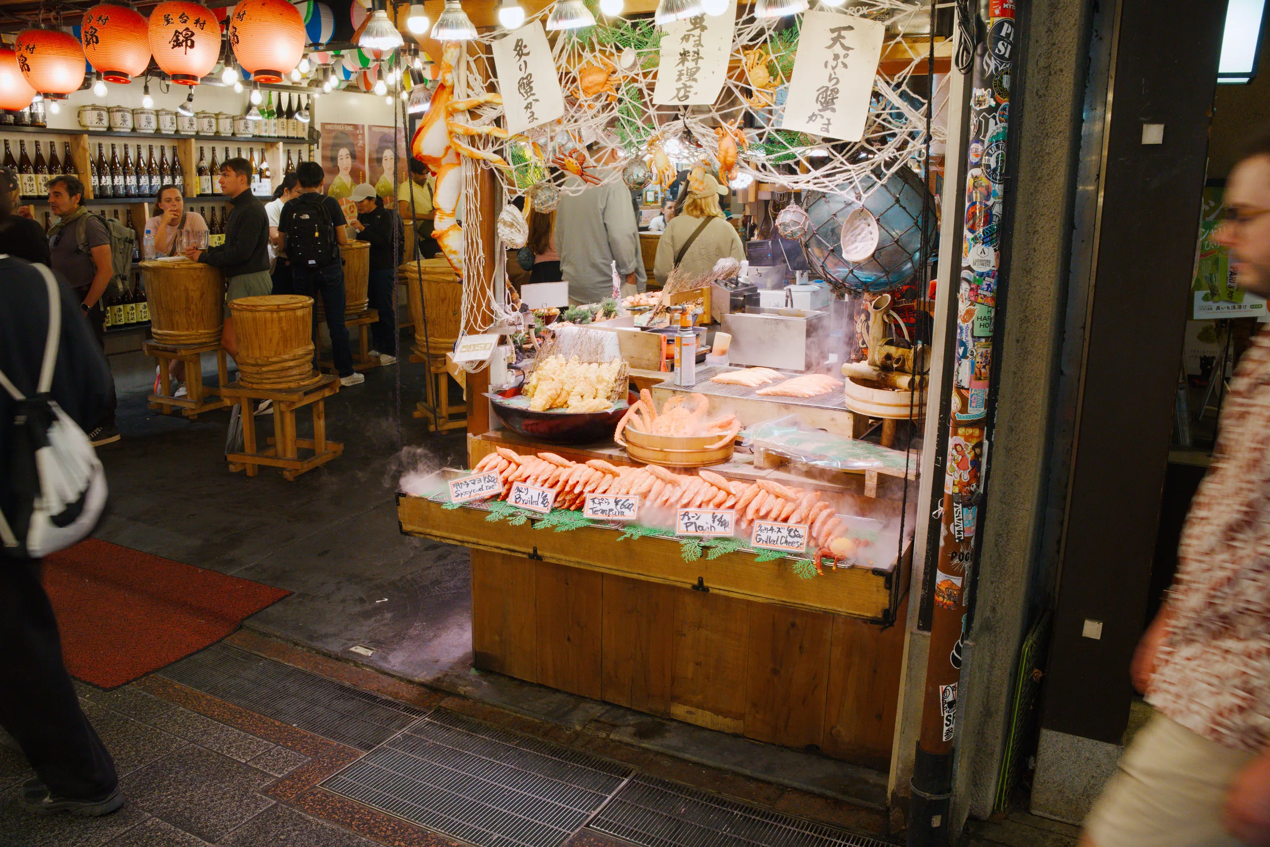 A shopkeeper tends a wooden counter display beneath red paper lanterns strung across the storefront opening.