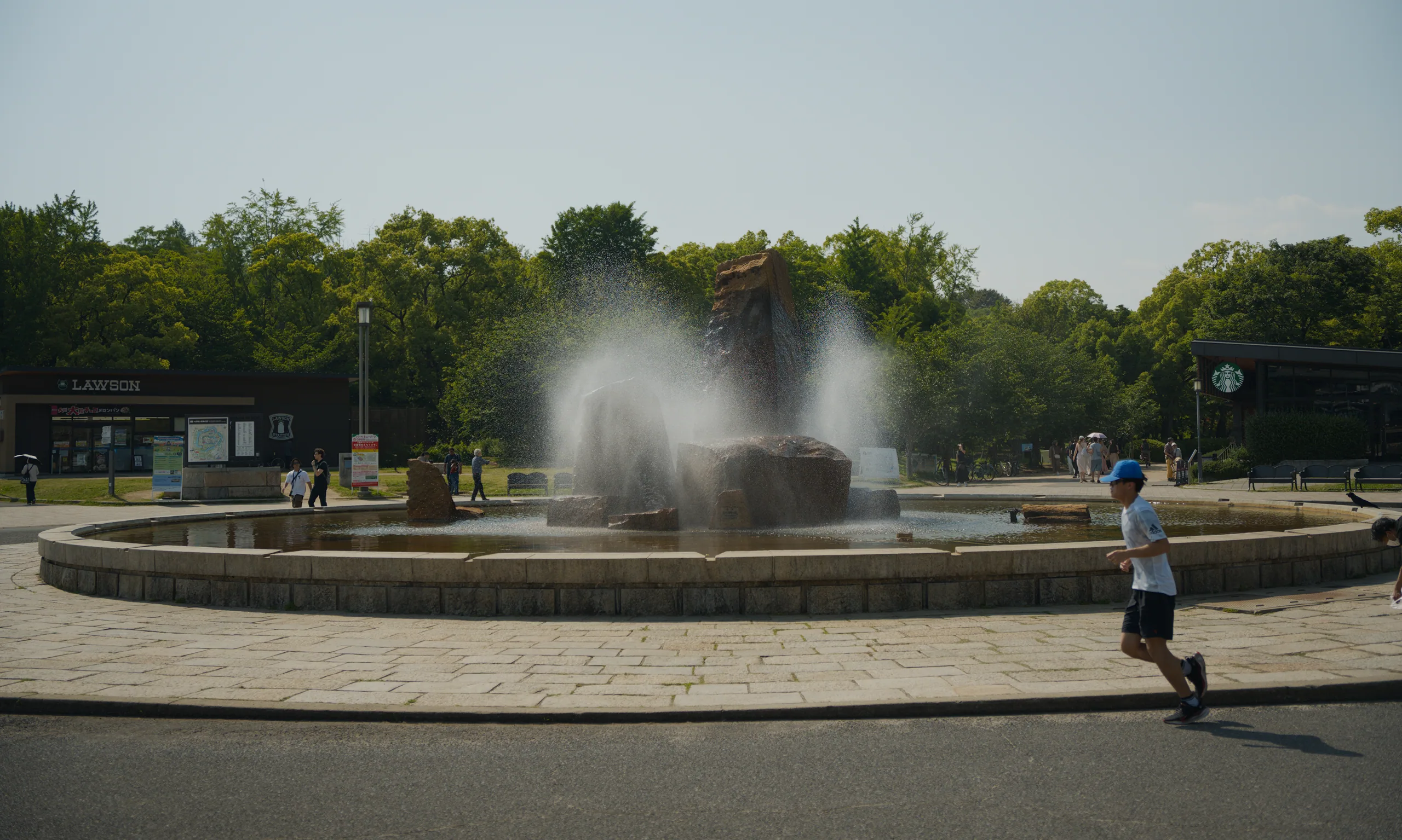 A circular fountain anchors a park with shade trees and open pathways.