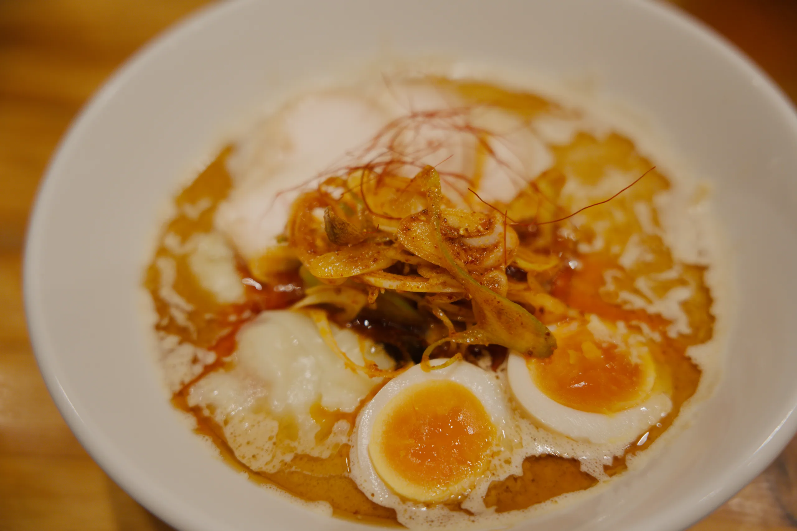 A close-up of a ramen bowl with sliced eggs and crispy fried toppings.
