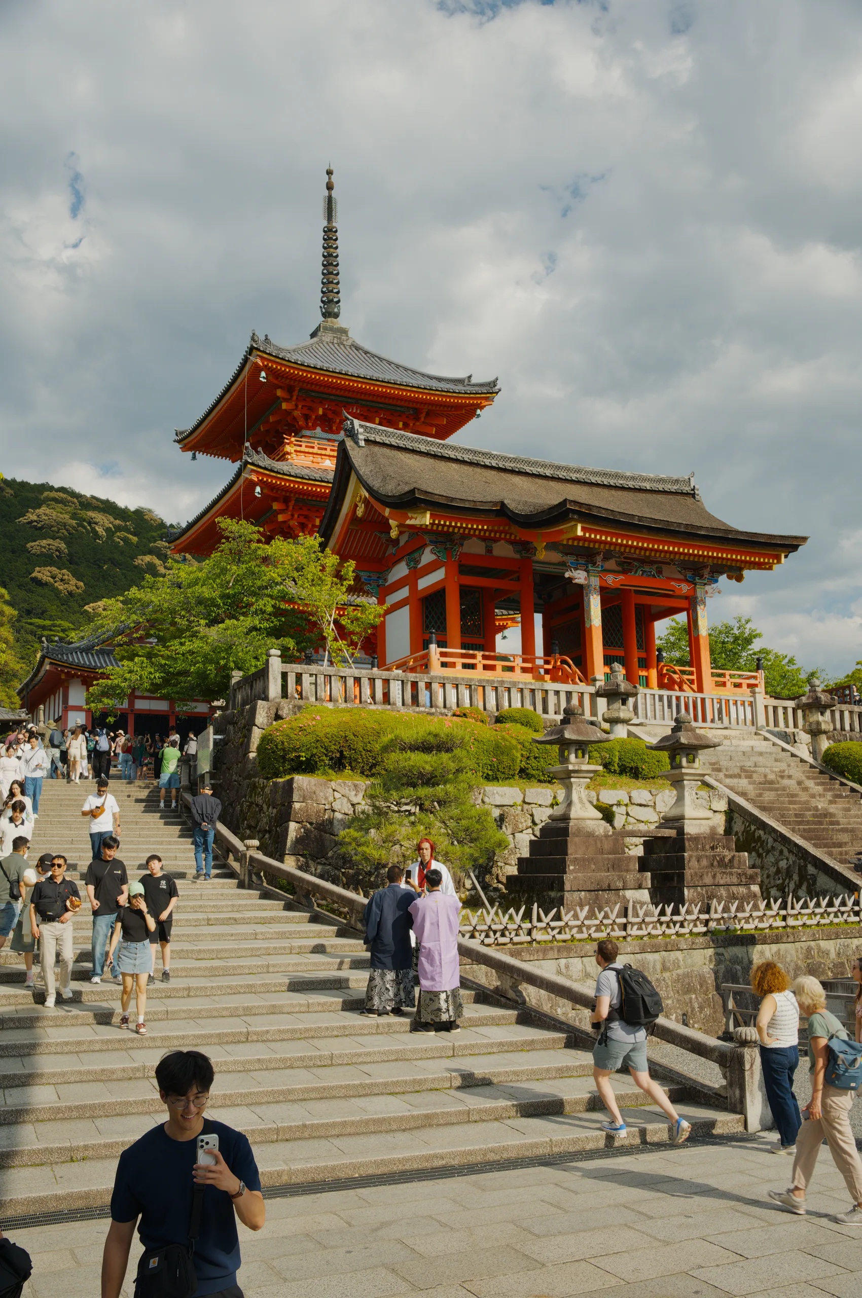 A broad stone staircase rises toward a red-roofed temple building with crowds ascending the steps.