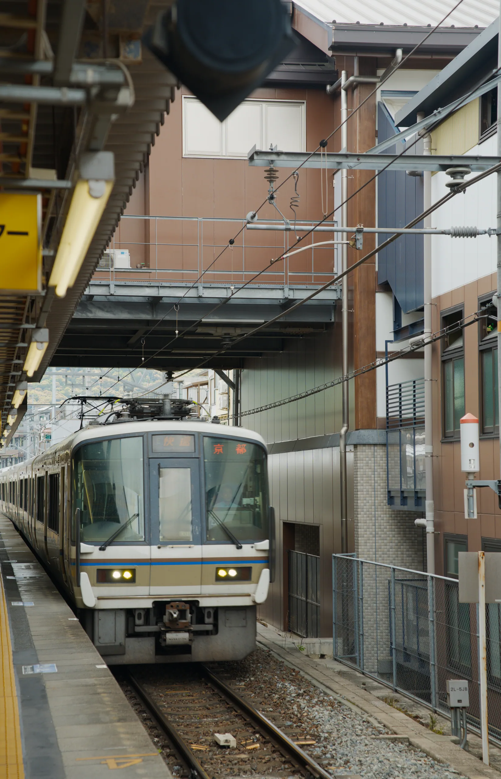 A cream-colored train with green trim stopped at a platform alongside brick buildings.