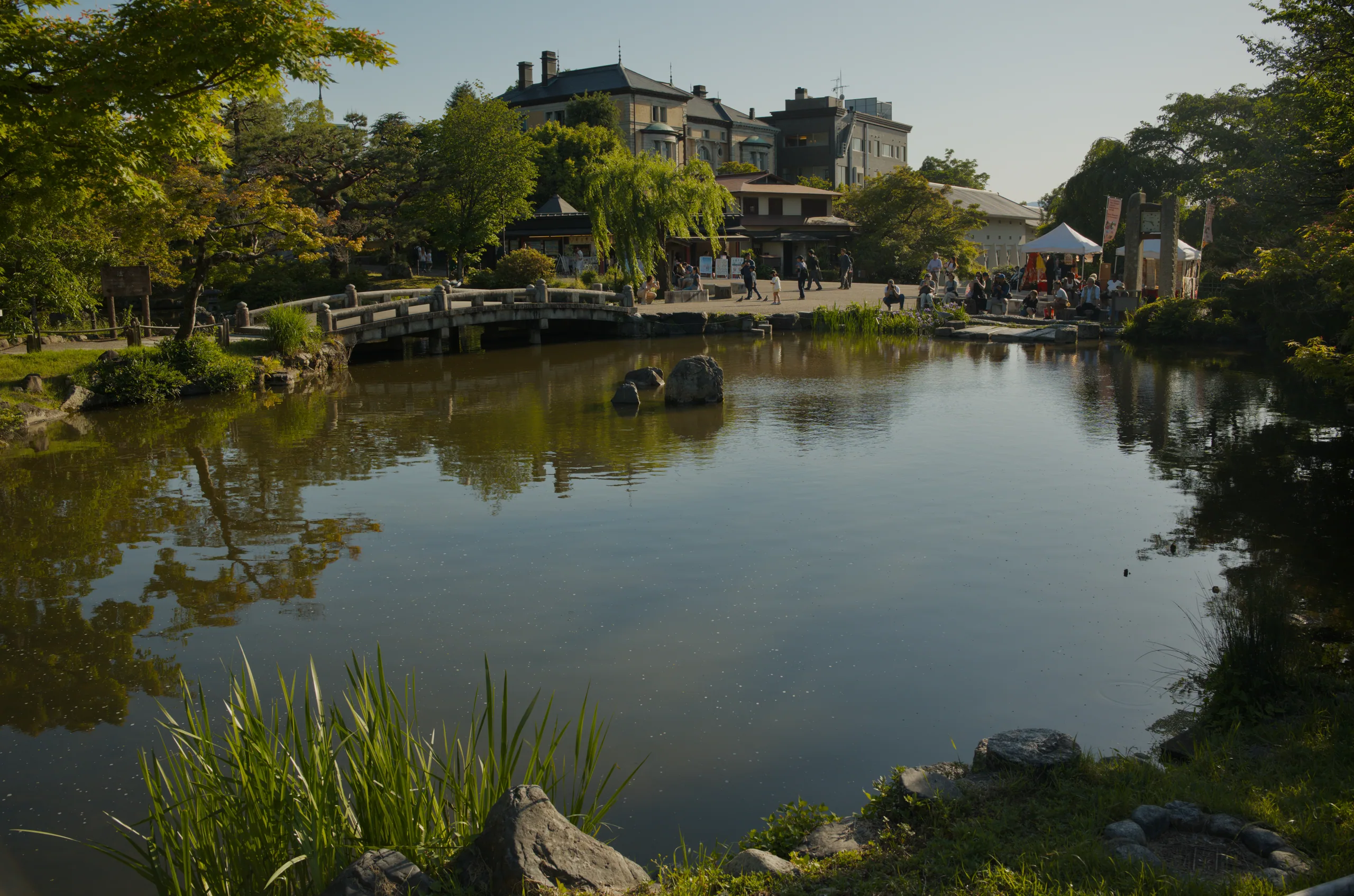 Stone buildings and tree-lined banks reflected in calm river water.