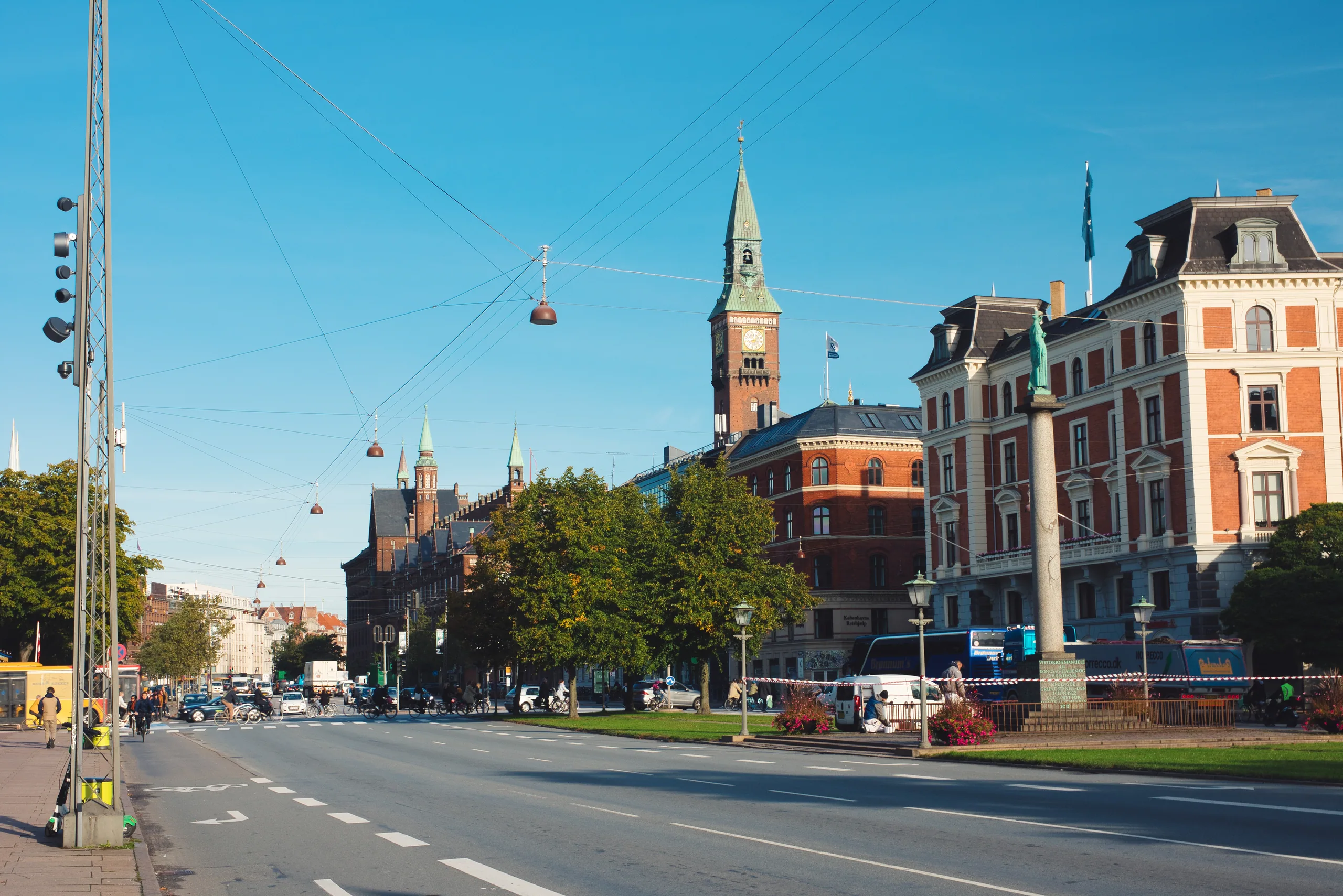 A broad Copenhagen street with cable-car gondolas strung overhead on wires, the city hall tower and ornate facades along the far side.