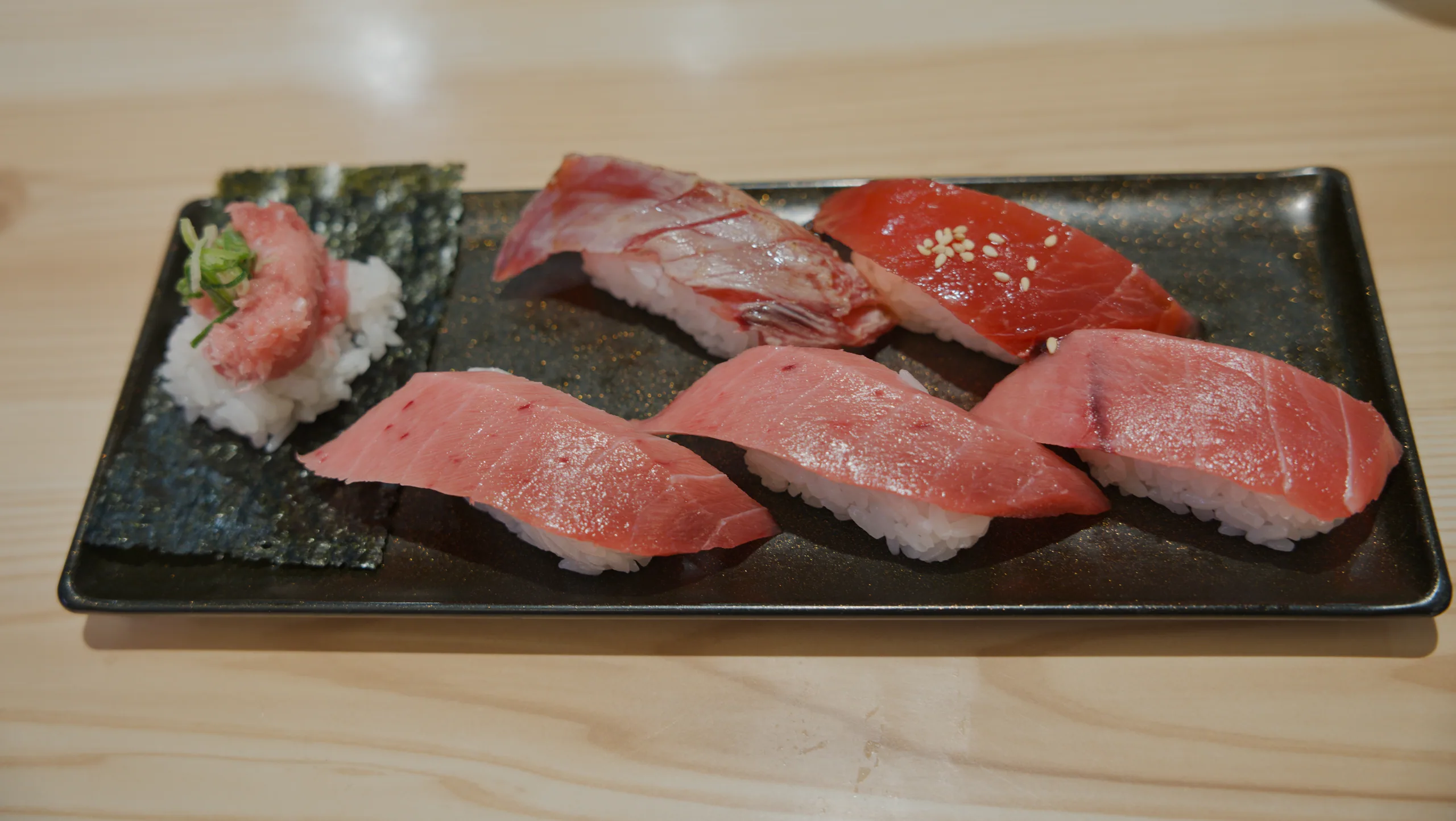 Raw fish pieces arranged on a dark rectangular plate with white garnish.