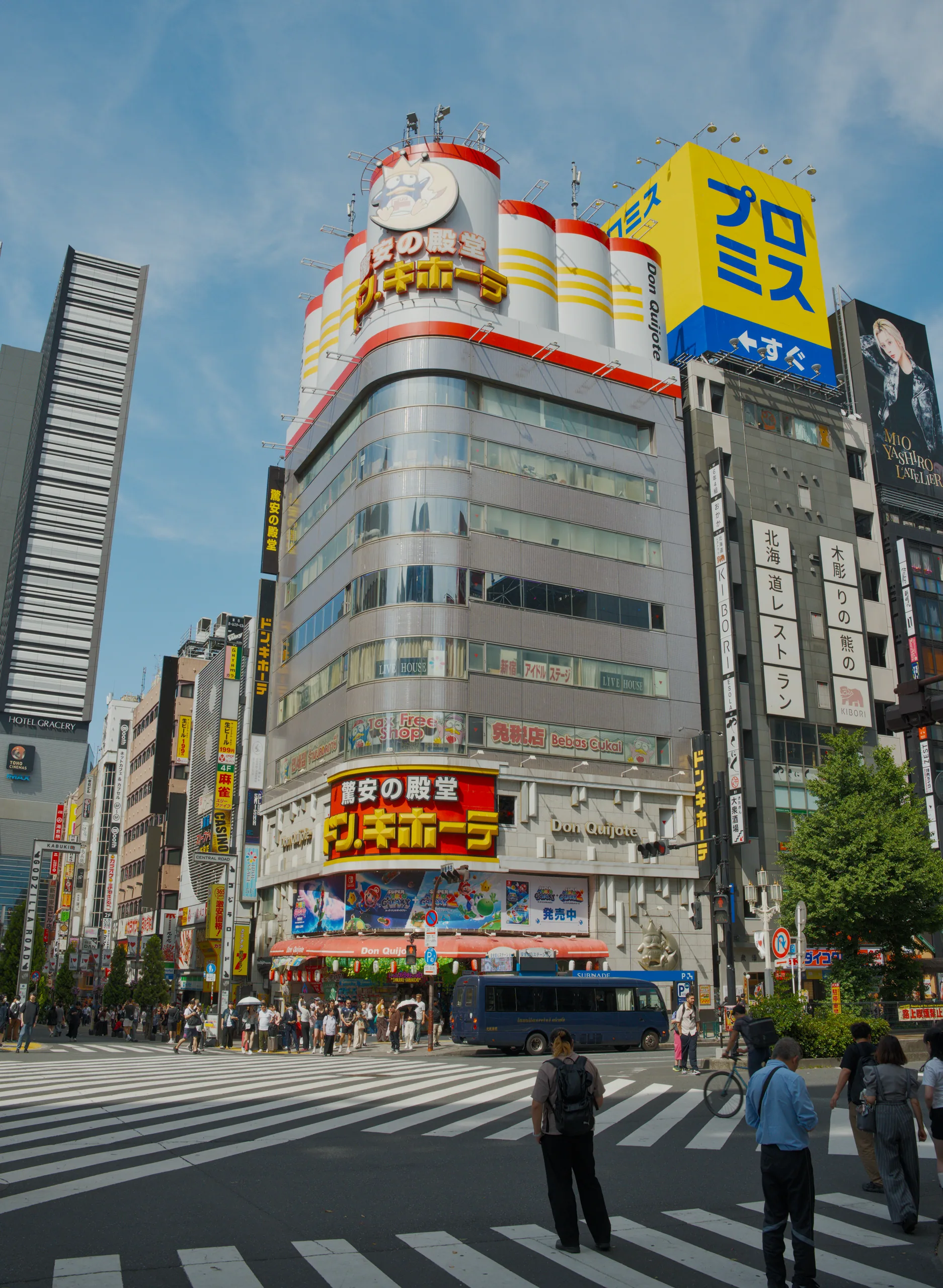 A busy intersection lined with colorful commercial building facades and a bus crossing at a crosswalk.