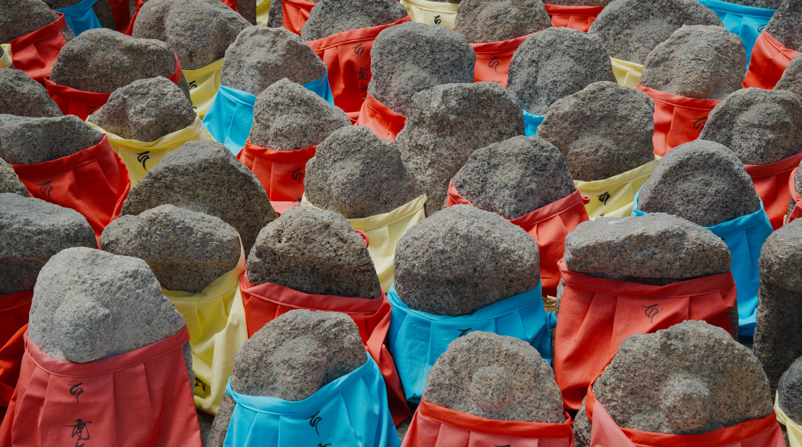 Large gray stone spheres with colorful cloth coverings in the foreground of an arranged installation.