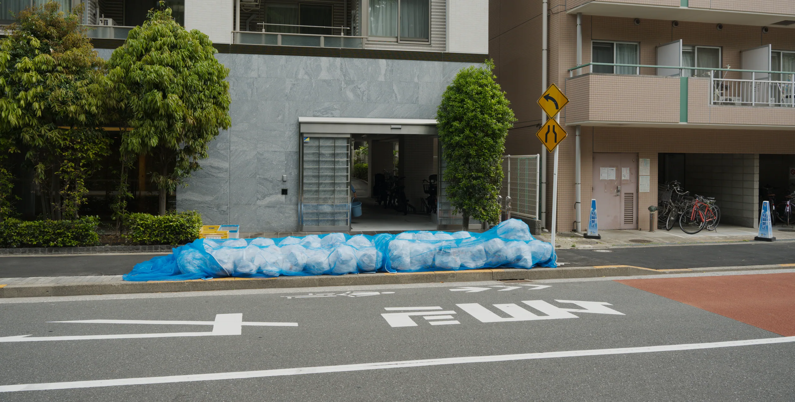 Bicycles parked along a street with blue-wrapped bundles and apartment buildings behind.