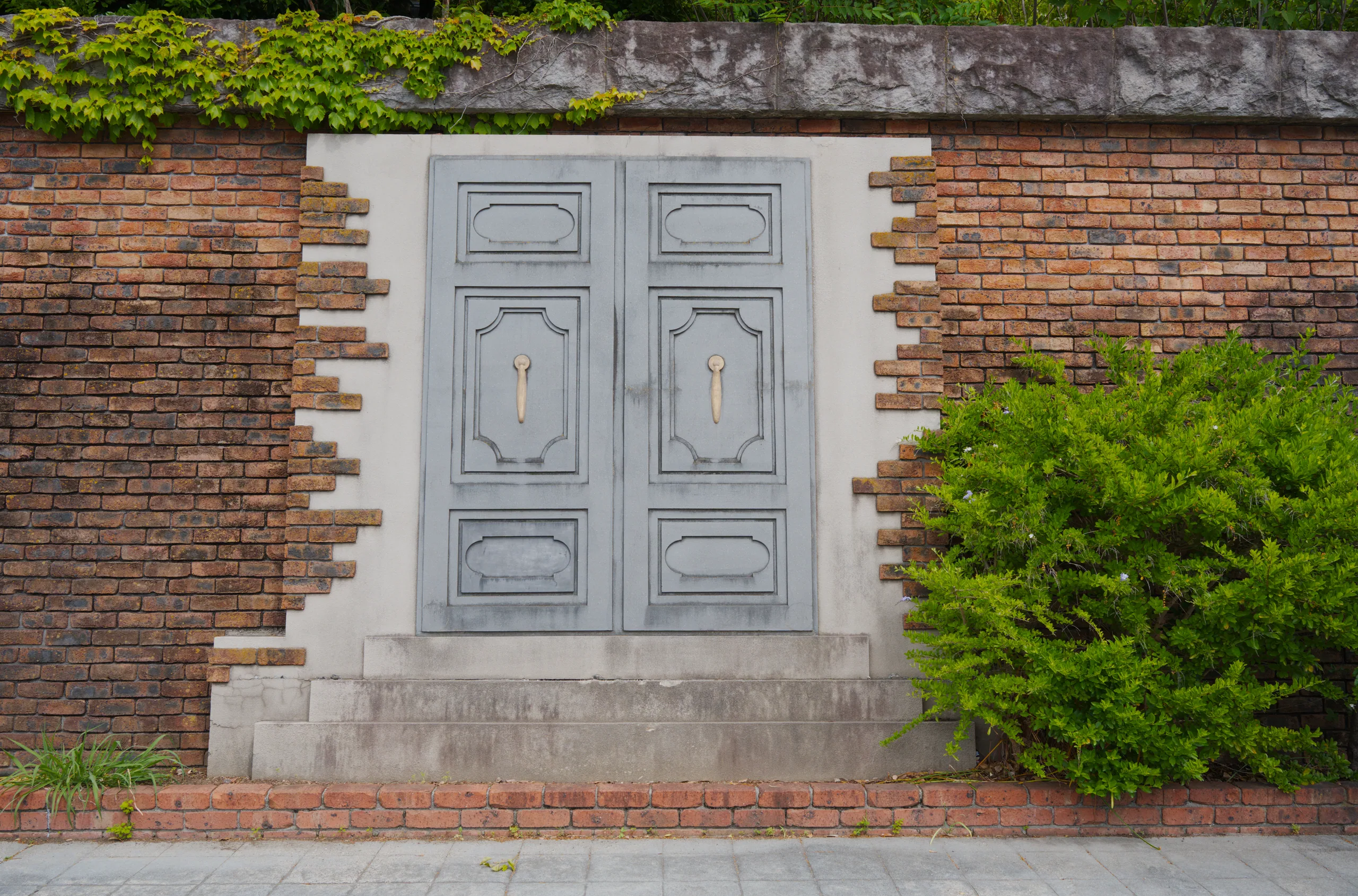 A white wooden door recessed in a brick wall with ivy climbing above and around it.