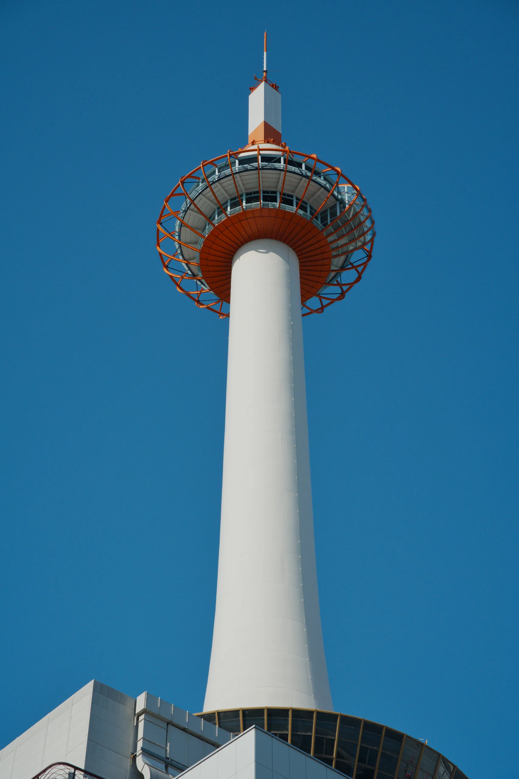 A white tower with a red circular disk structure against clear blue sky.