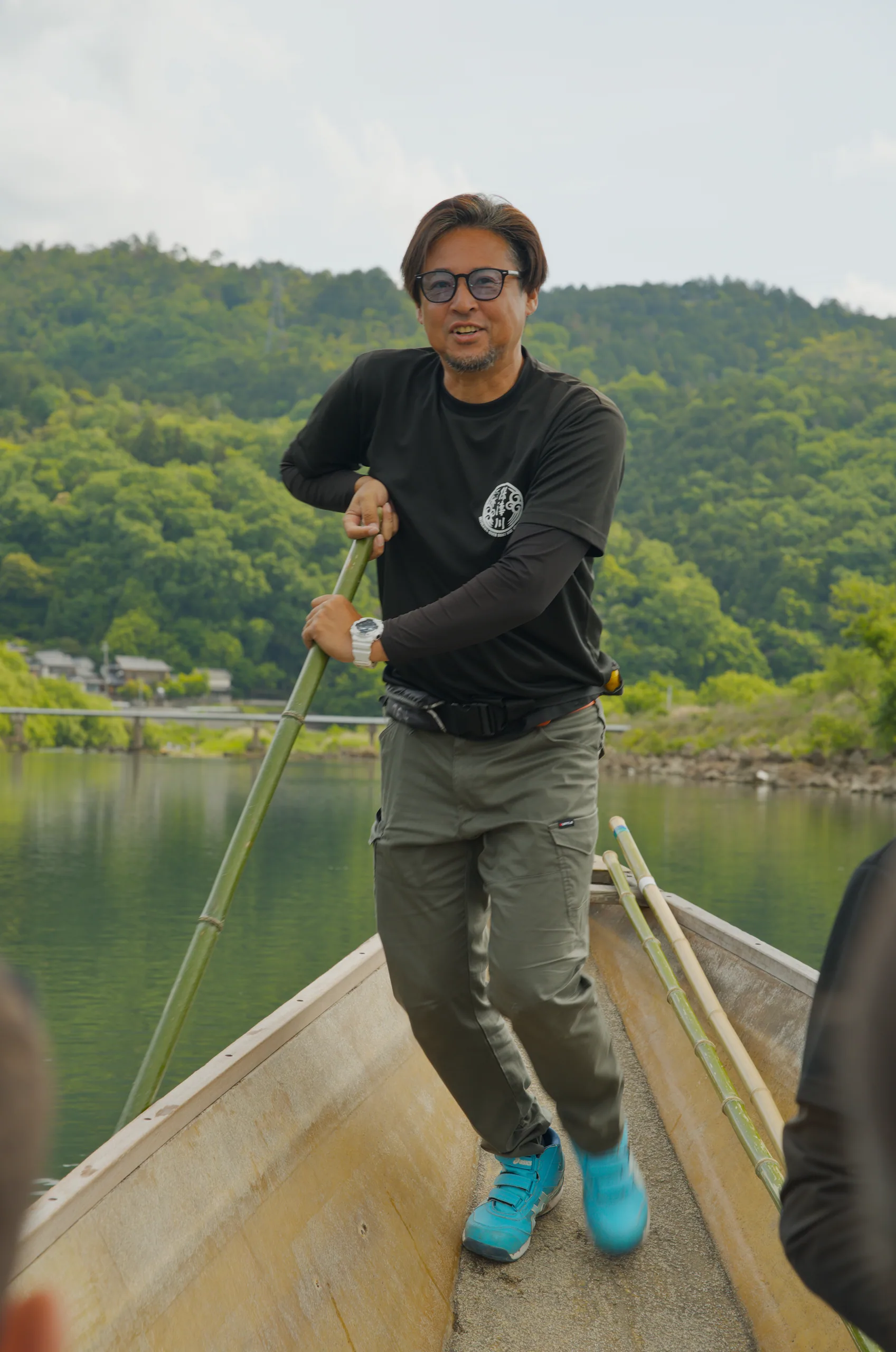 Person paddling a boat down a river with forested hills rising behind.