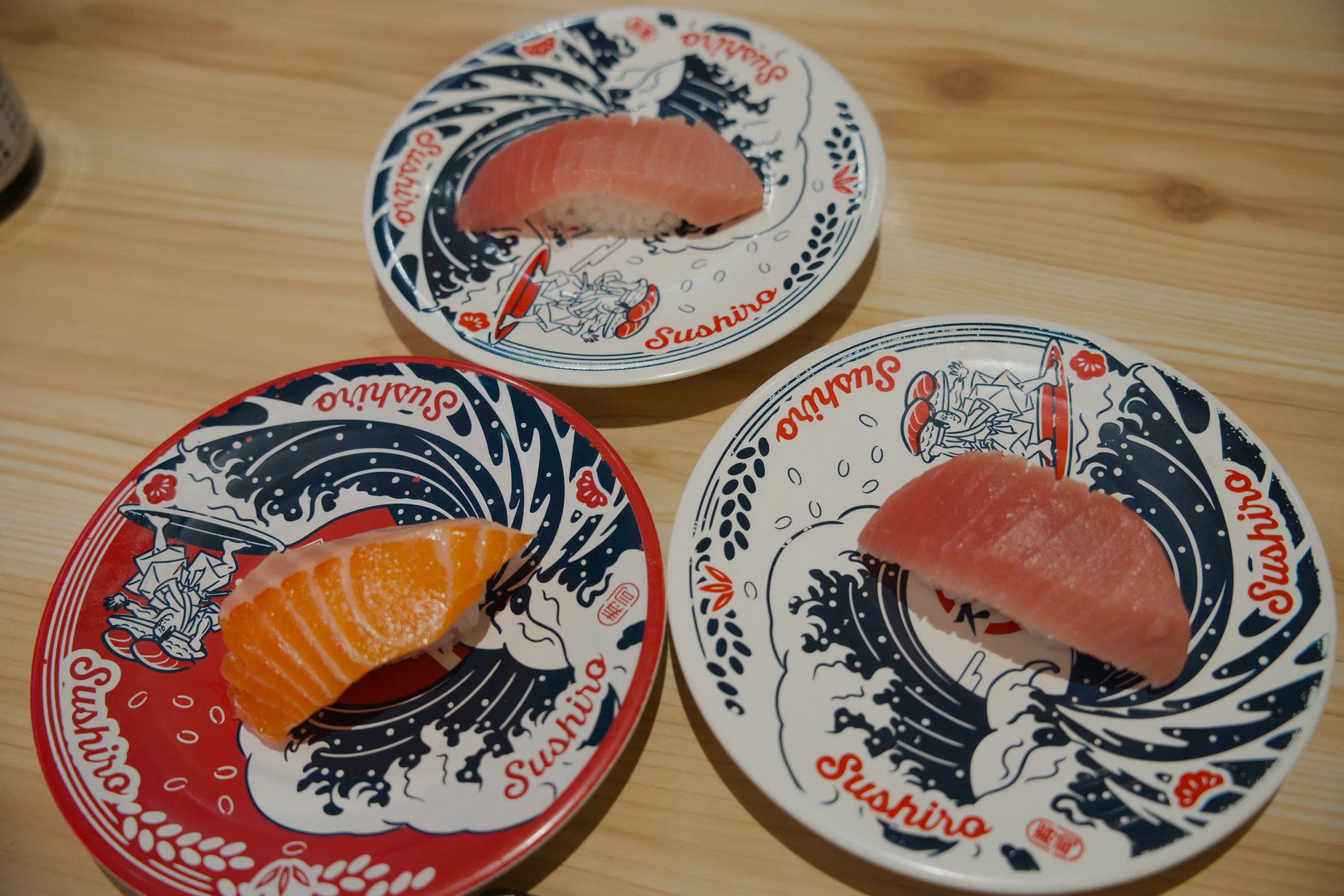 Three porcelain dishes with red and blue painted designs holding fish pieces on a wooden surface.