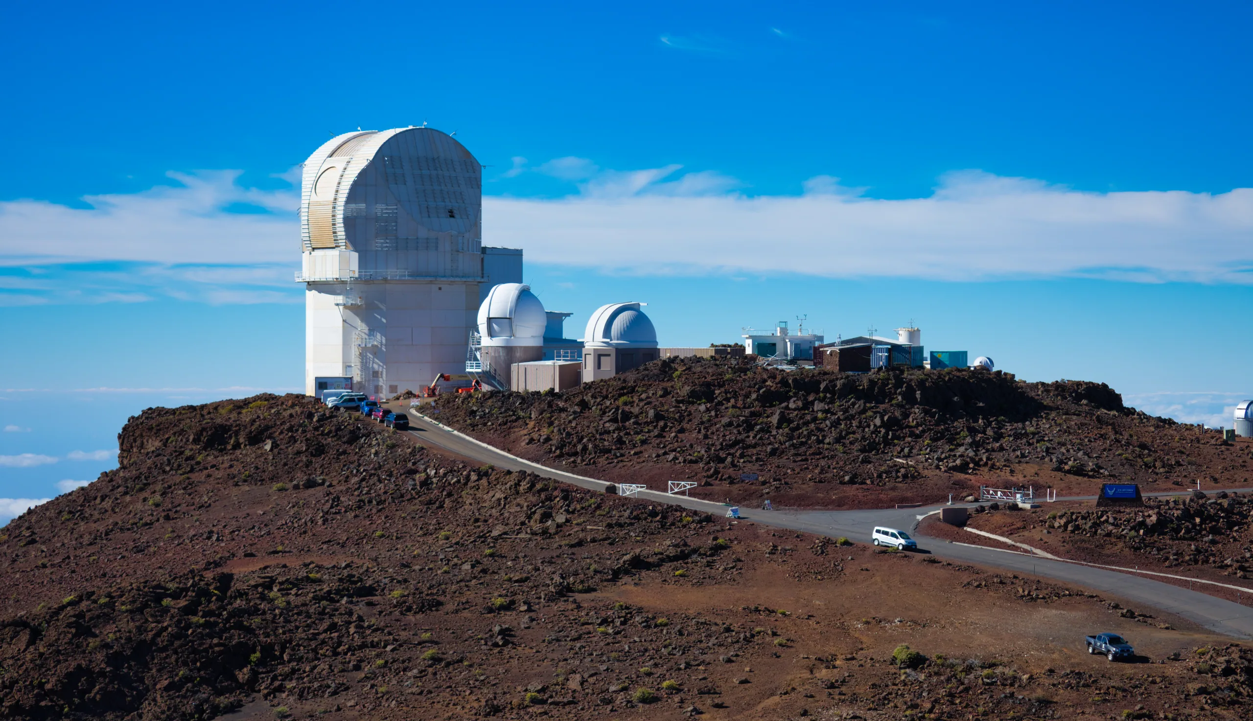White observatory domes on a bare volcanic summit, a road curving up to them under a blue sky.