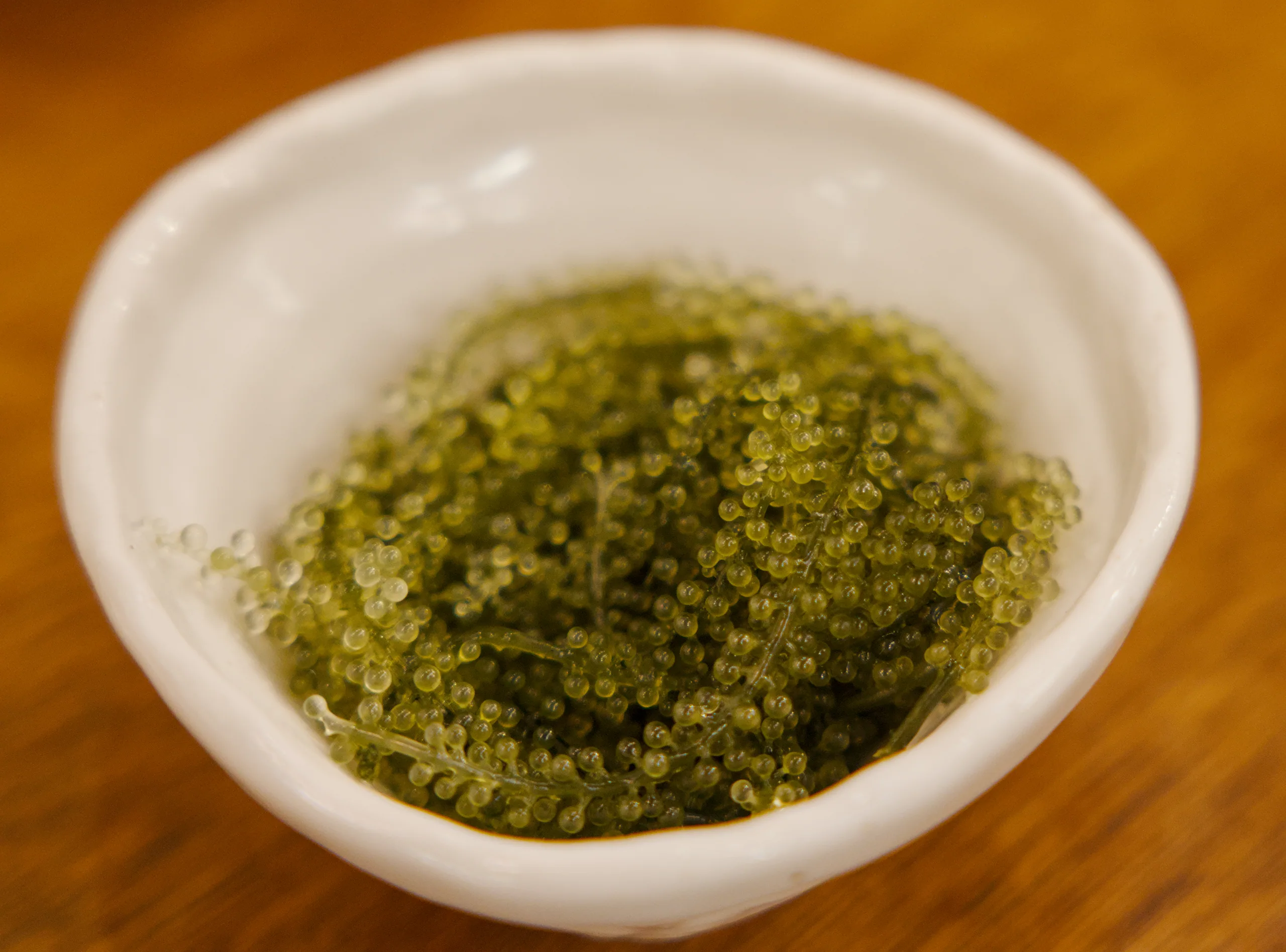 White bowl of bright green sauce or pesto on a wooden table surface.