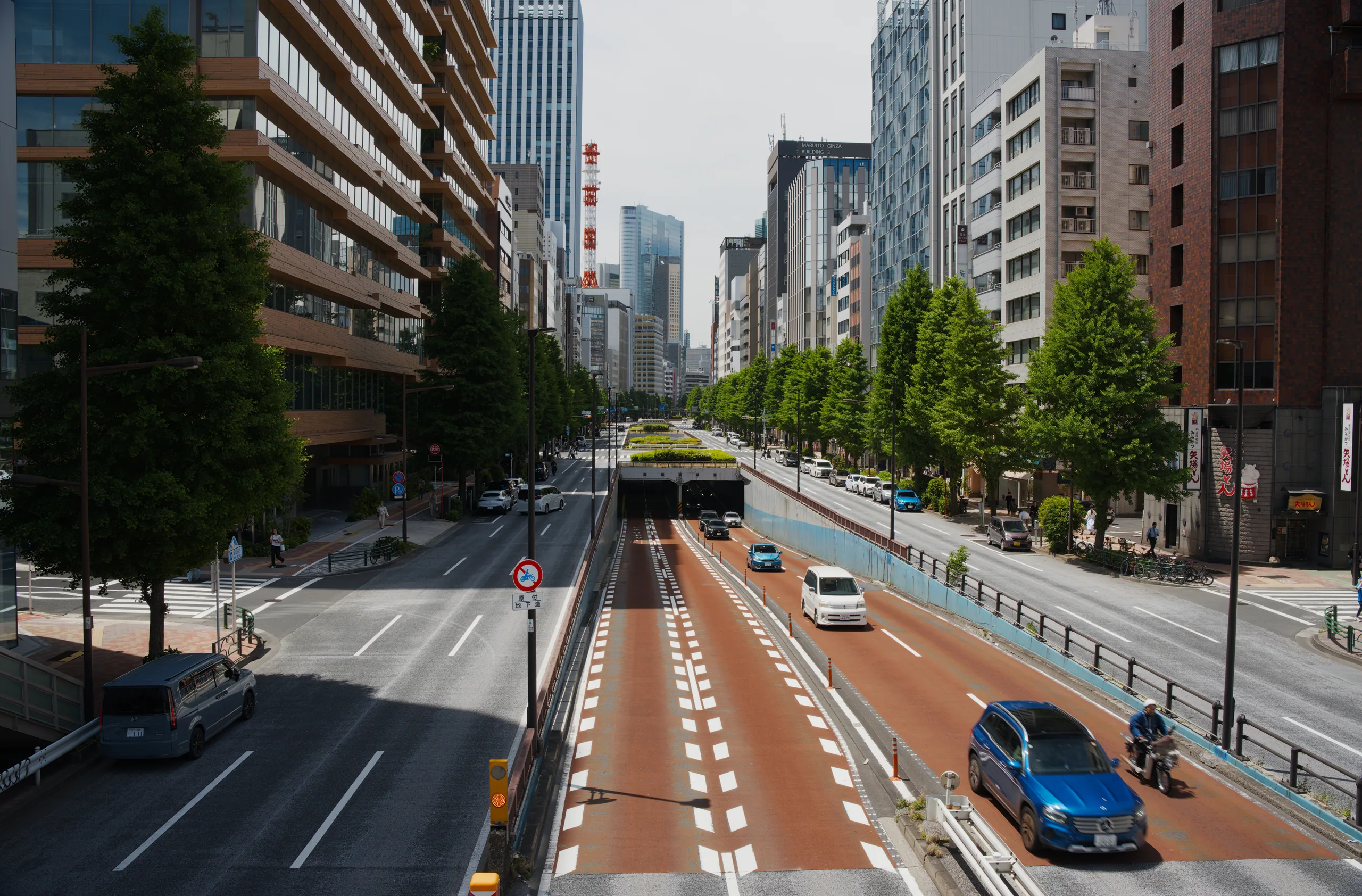An elevated view of an urban intersection with traffic, crosswalks, tree-lined streets, and tall buildings.