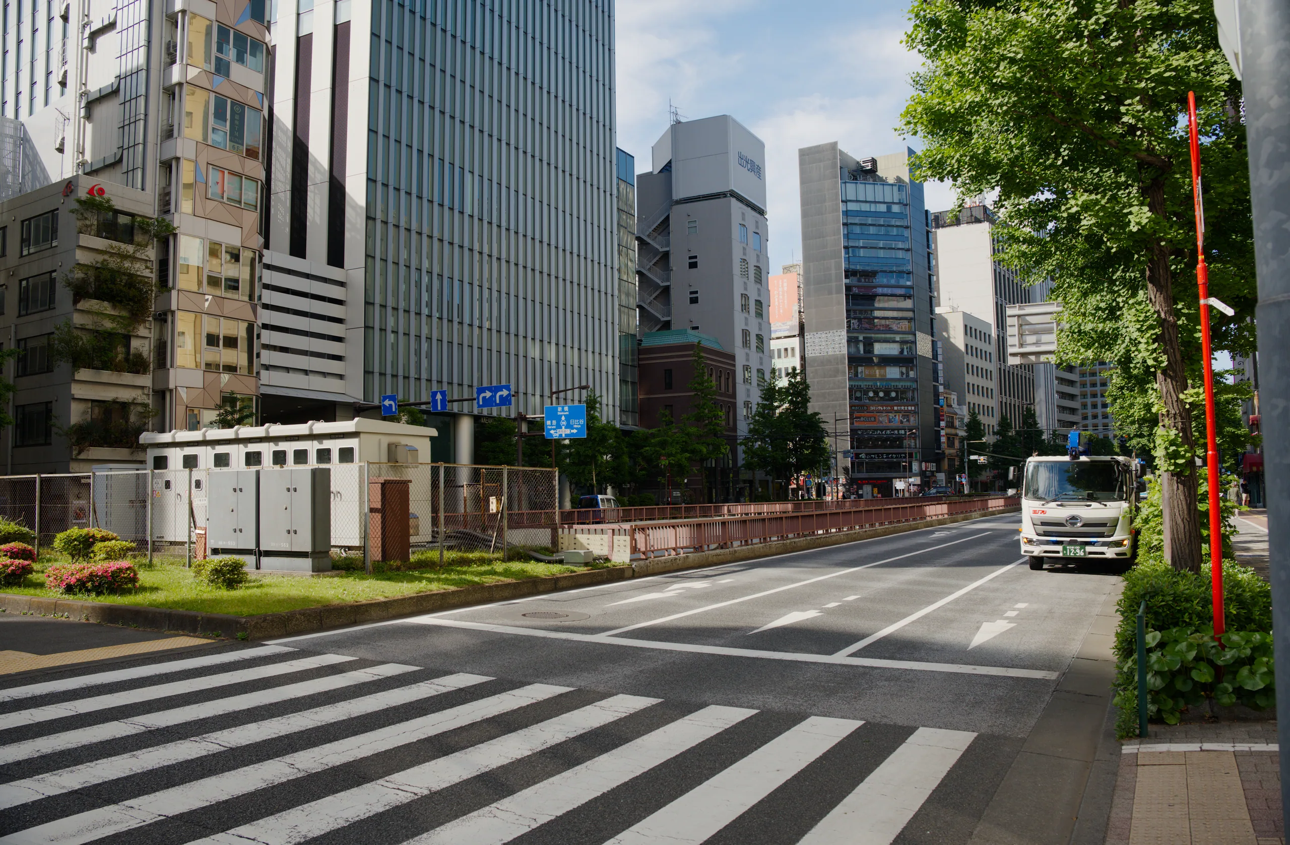 Wide urban street with multiple zebra crossings and office buildings under partly cloudy sky.