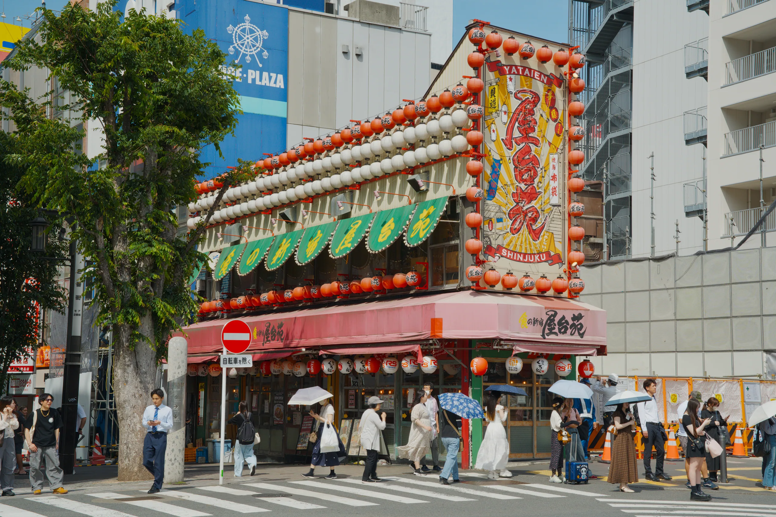A red and gold shopfront with Japanese architectural details stands above a crosswalk where pedestrians gather.