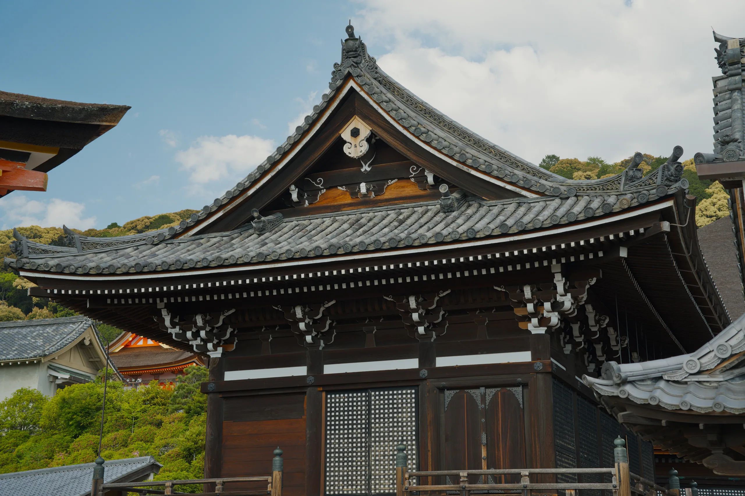 Black wooden Japanese temple with curved roof and forested hillside beyond.