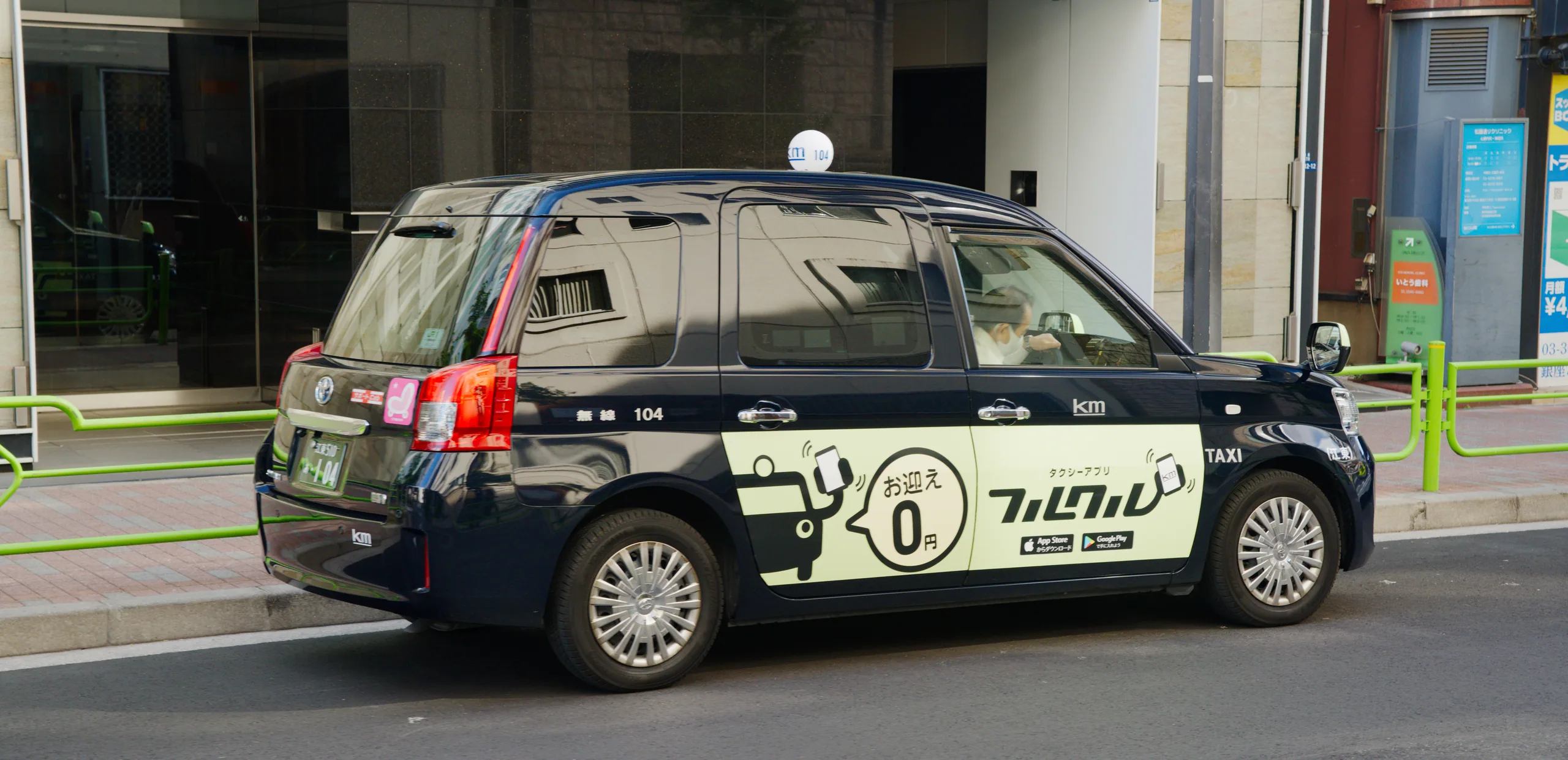 A black commercial vehicle with Japanese characters sits parked on an urban street with modern buildings.