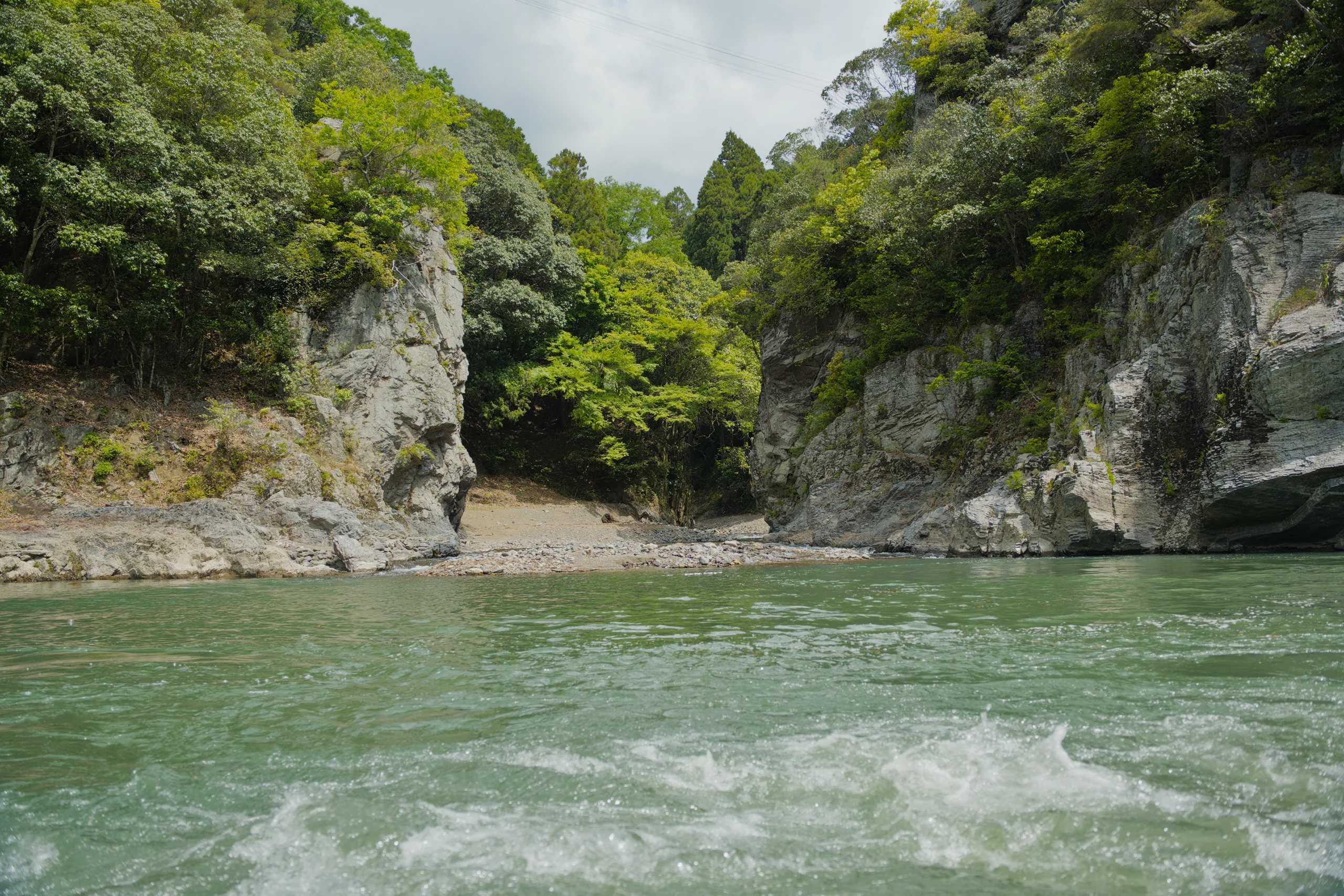 A river flows through a narrow gorge with steep rocky banks covered in green vegetation.