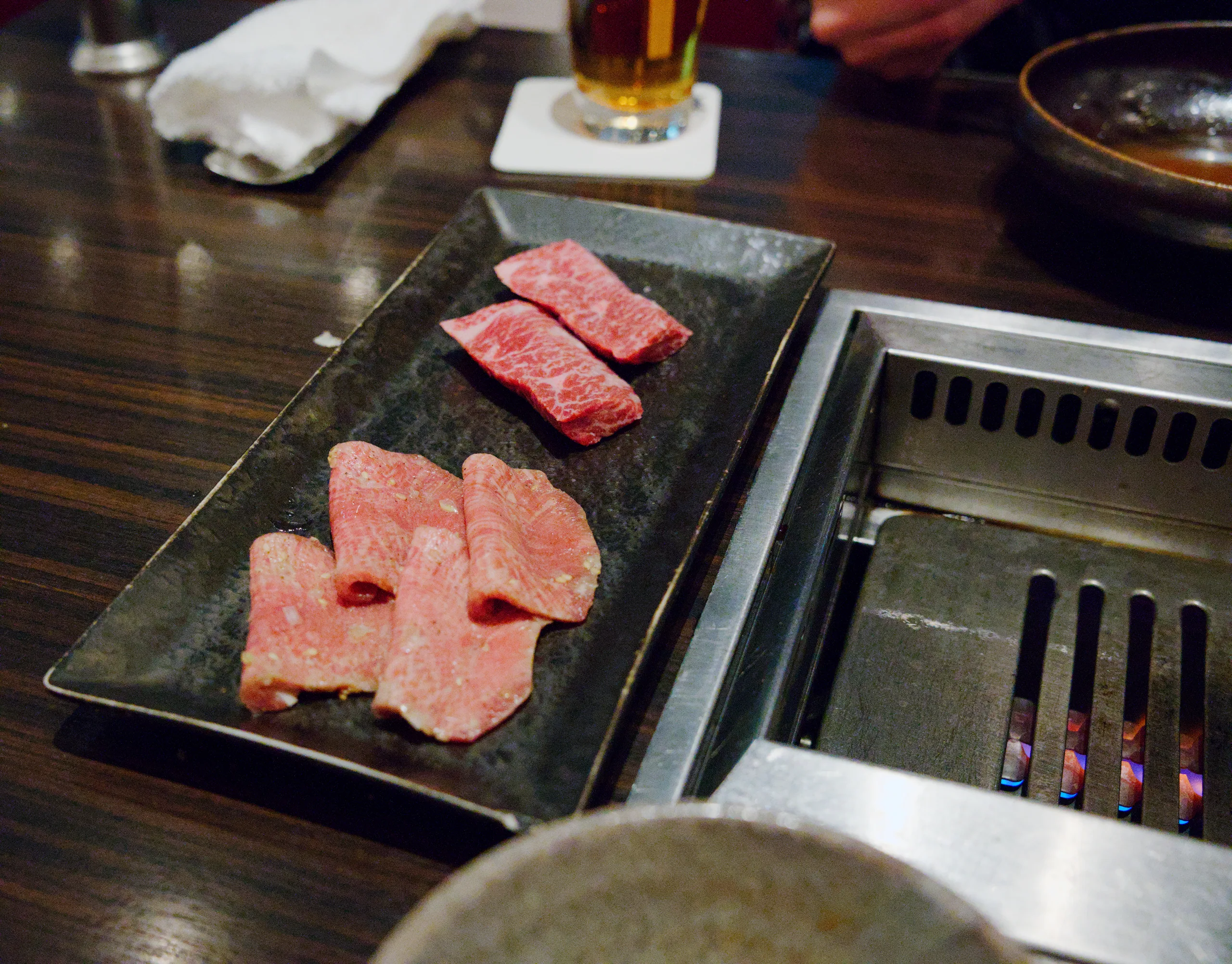 Sliced raw meat is arranged on a black slate plate on a wooden table.