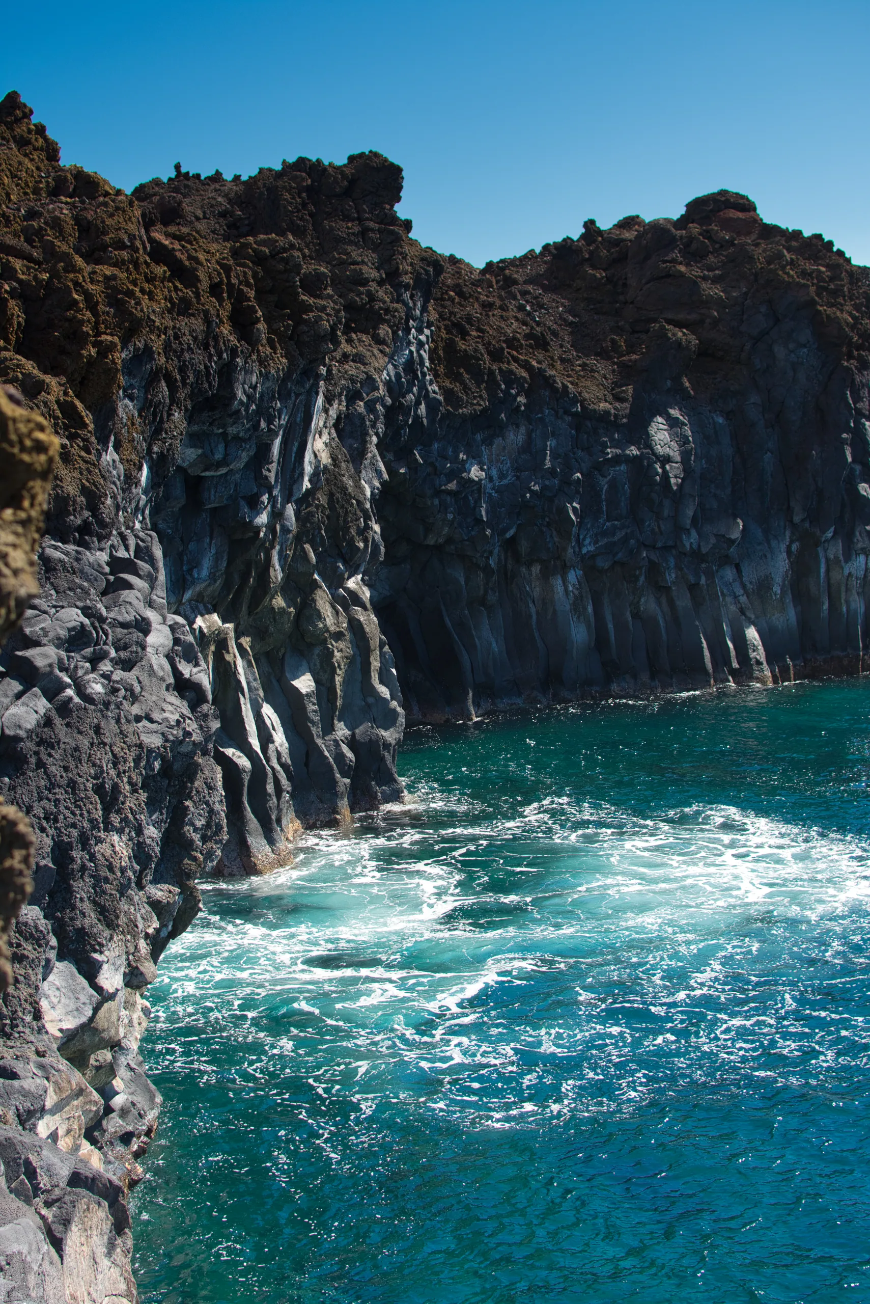 White water churning in a narrow inlet at the foot of tall basalt sea cliffs.