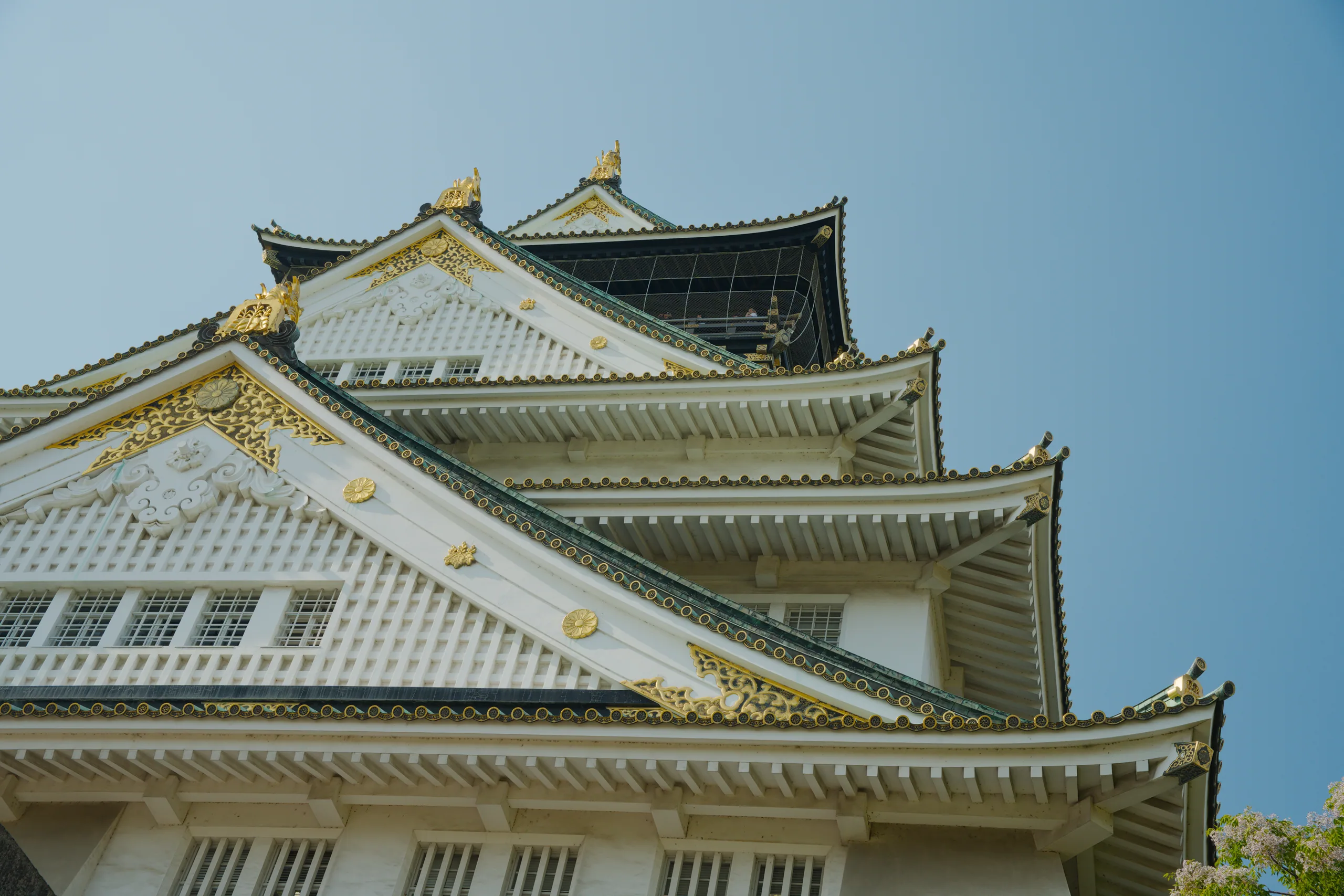 Multi-tiered white and gold castle roofs with curved, upturned eaves against a clear blue sky.