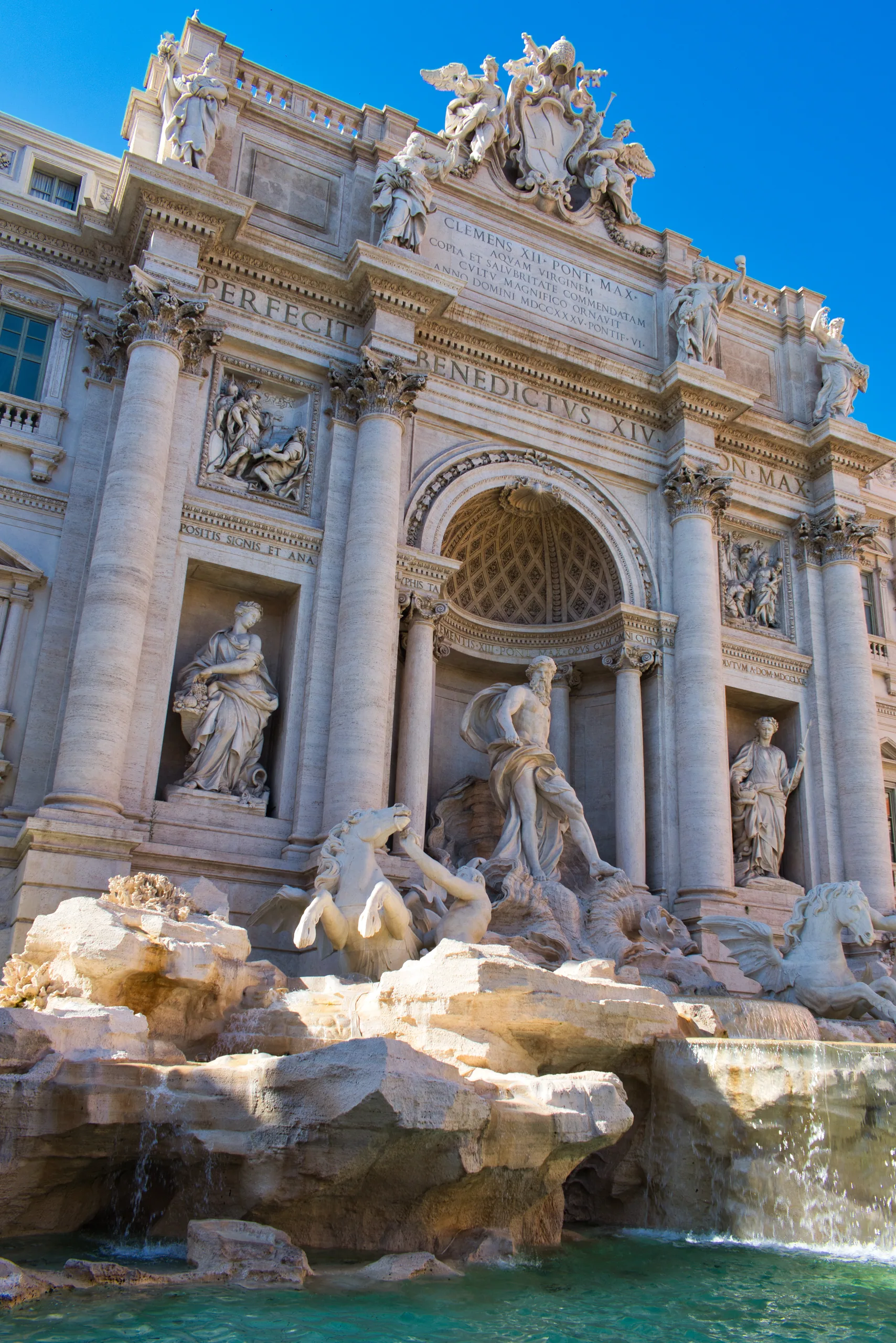 The Trevi Fountain seen from below, its marble figures and rearing horses under a deep blue sky.