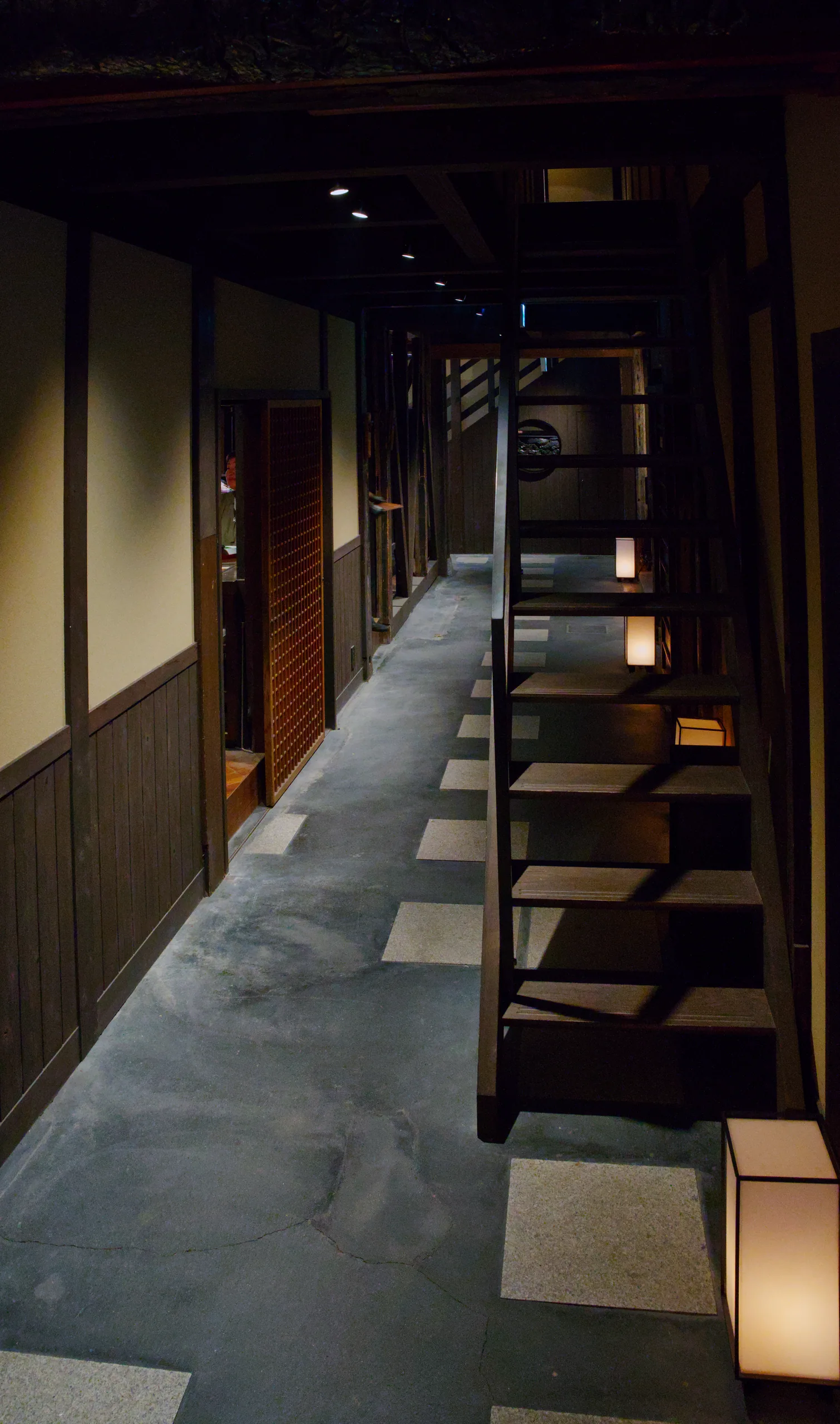 A wooden-paneled hallway lit by paper lanterns receding into shadow.