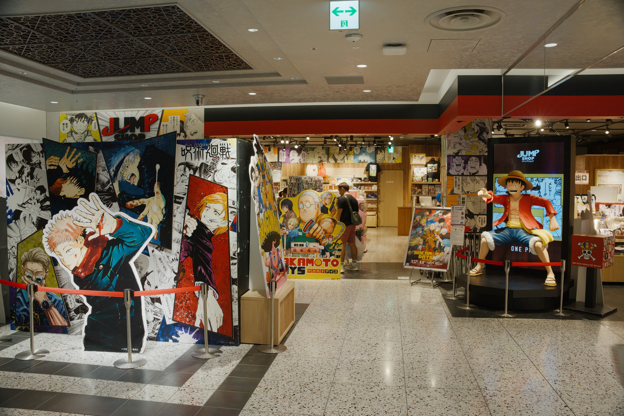A shopping arcade interior with Japanese anime and character merchandise displayed in storefronts.
