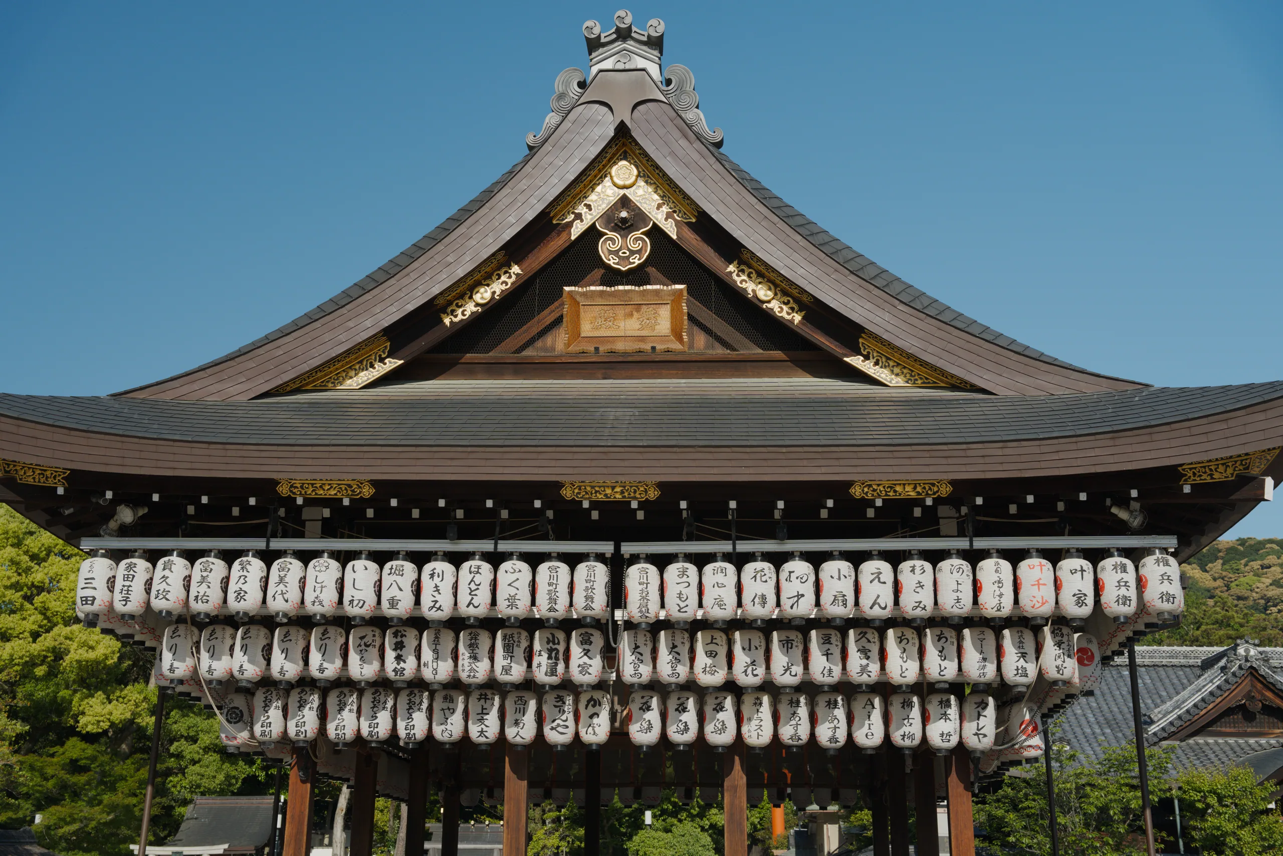 Traditional Japanese shrine with ornate peaked roof and hanging lanterns beneath the eaves.