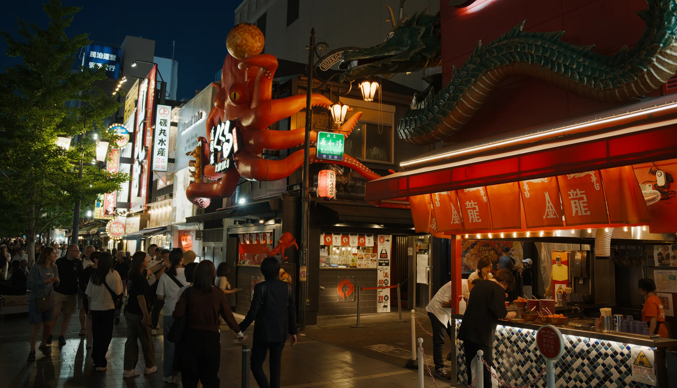 Storefronts with neon signage and illuminated signs along a nighttime street in an urban district.