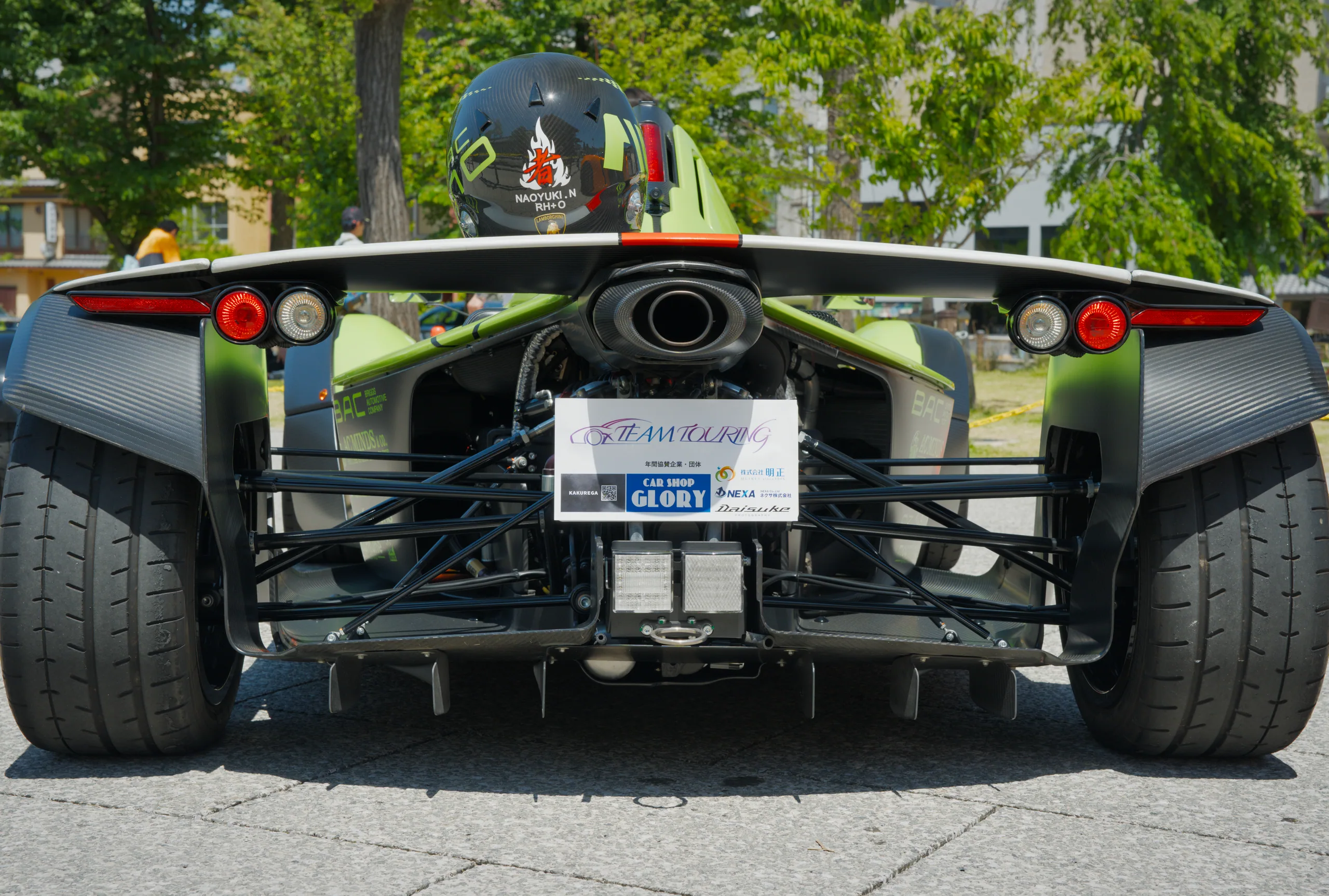 Rear view of a race car at a car show, with spectators and other vehicles in the background.