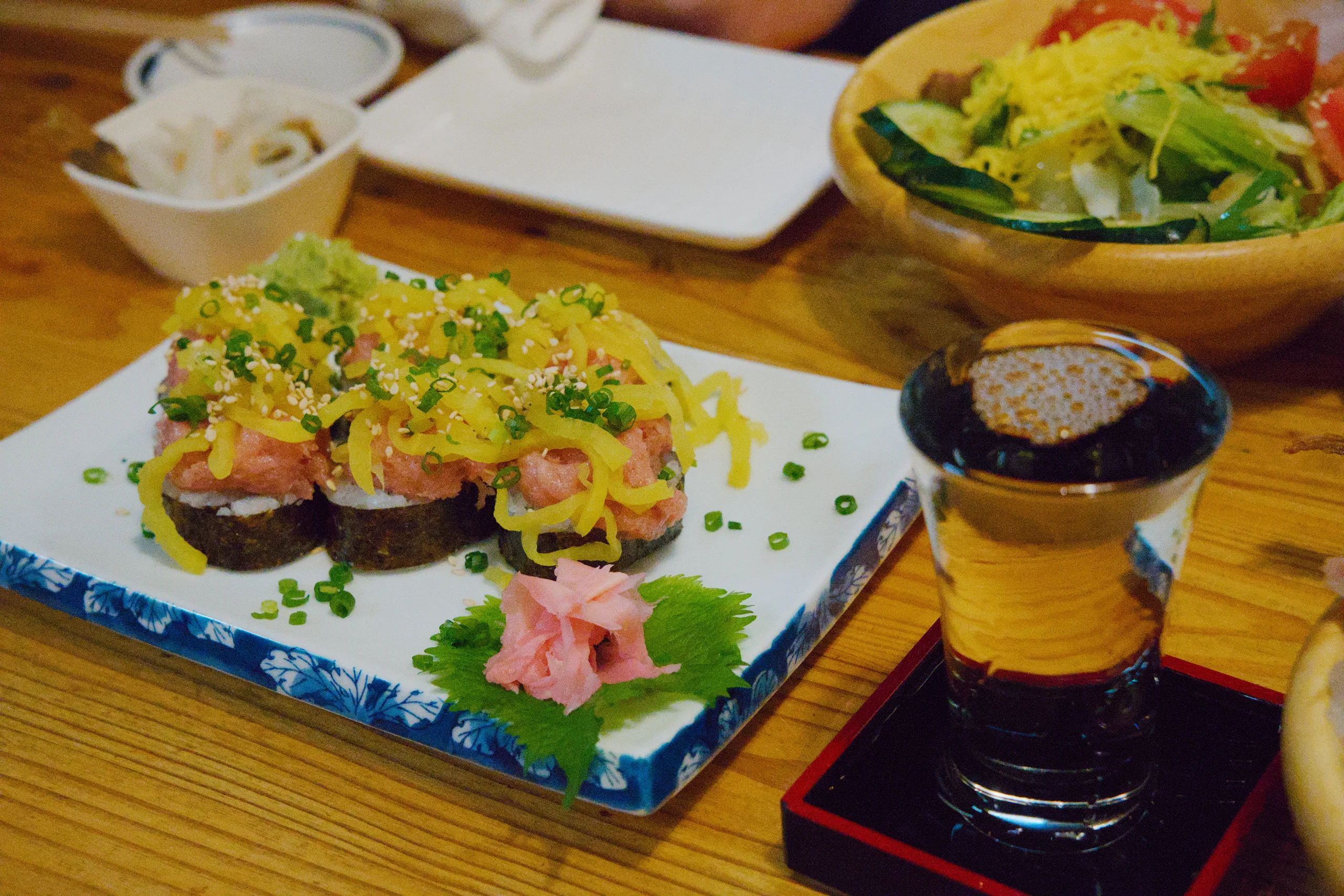 Prepared dish with green herb garnish on a decorated plate, sauce container positioned beside it on a wooden table.
