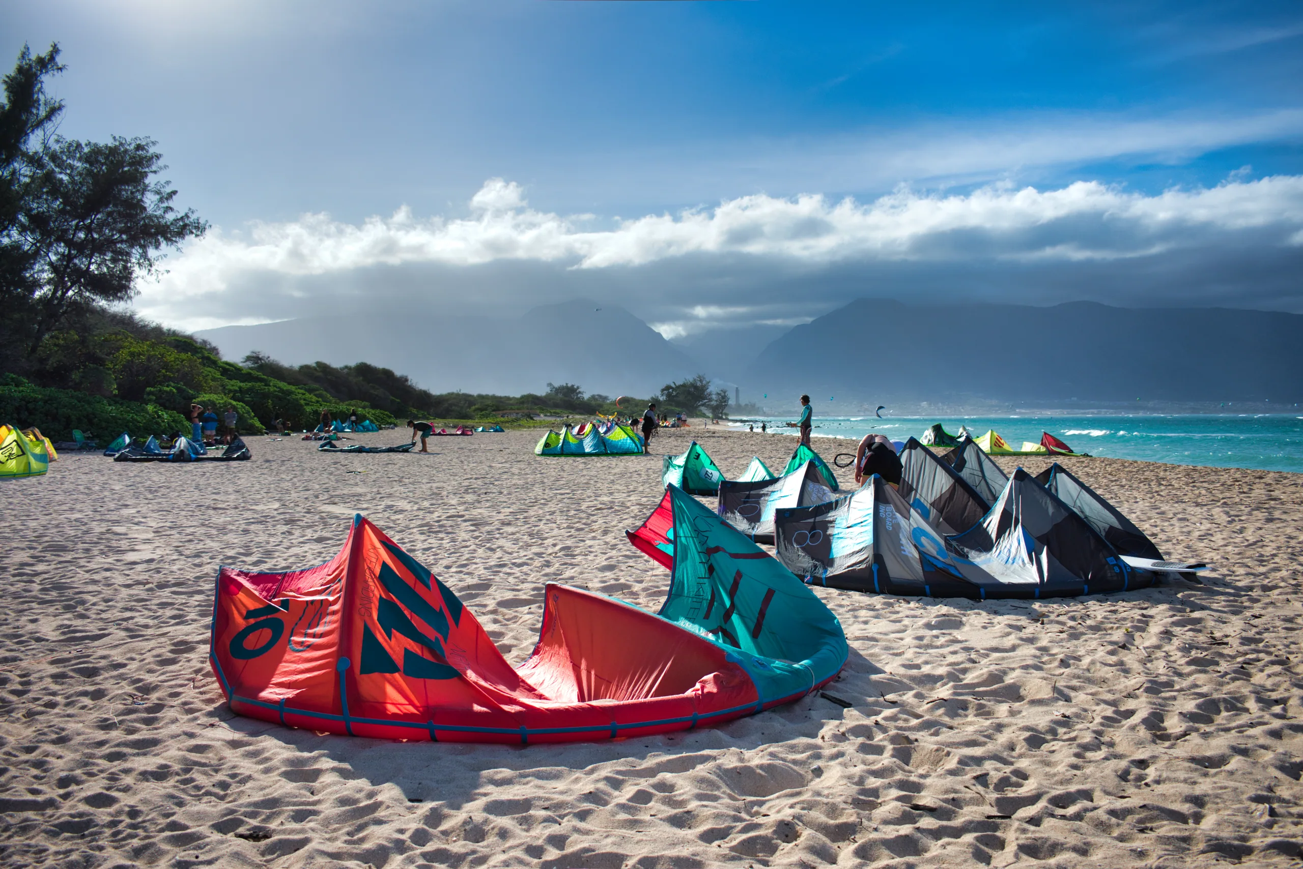 Kitesurfing kites laid out across the sand at Kanaha beach, mountains and cloud along the coast behind.