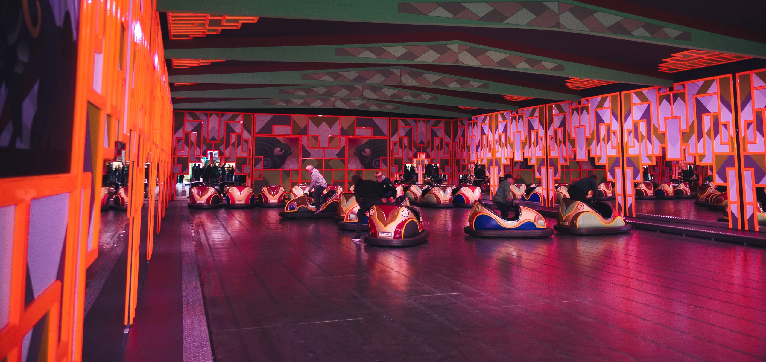 An empty bumper car rink lit in saturated pink and orange, the cars parked in rows across the floor.