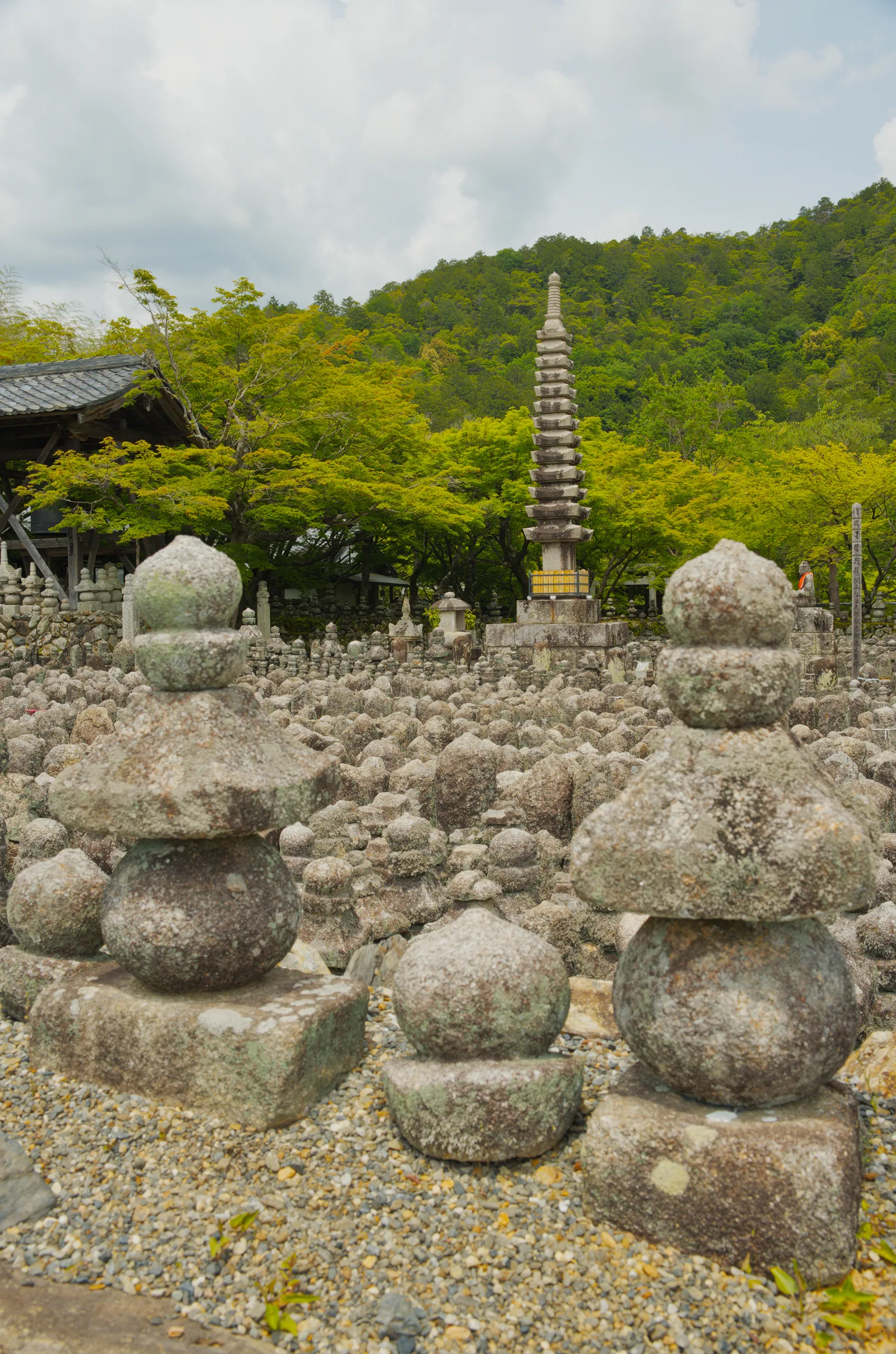A stone pagoda stands among large rounded boulders in a terraced garden backed by forested hills.