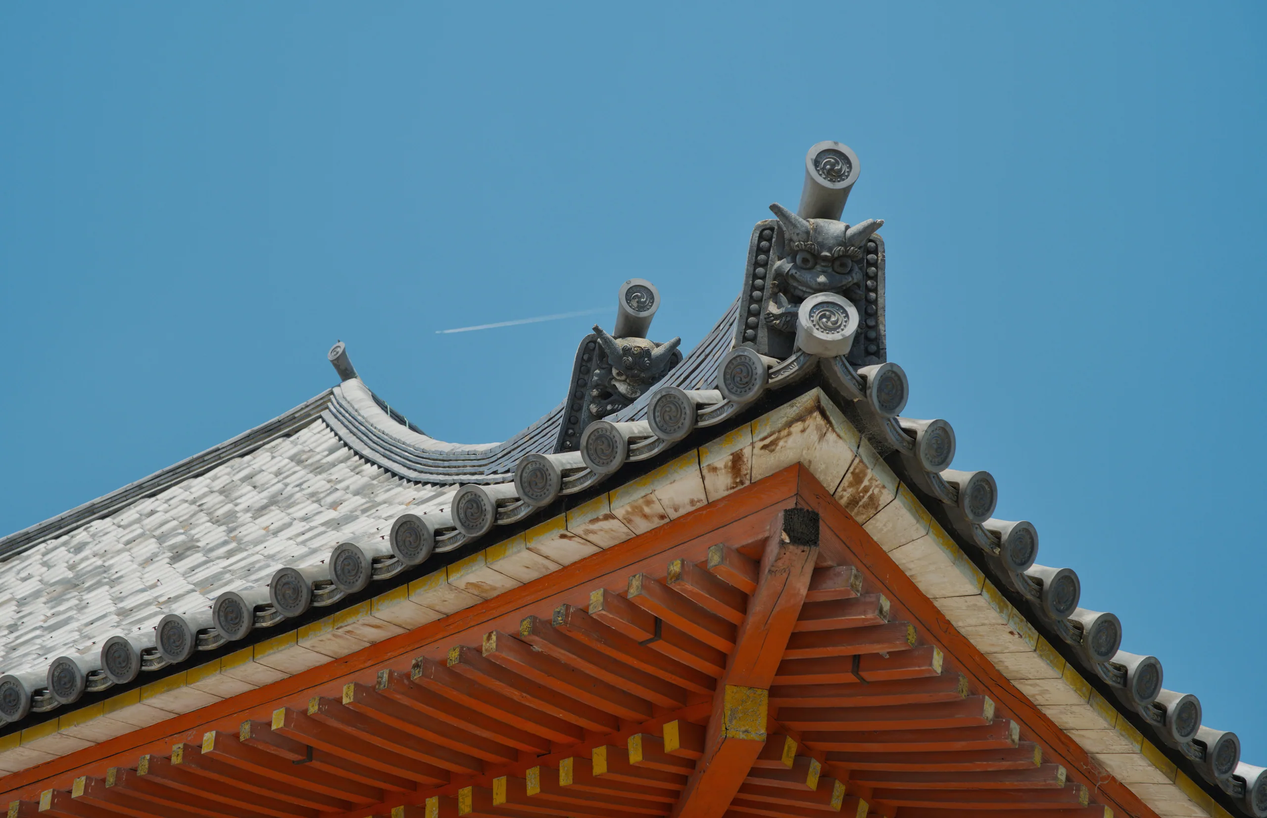 Ornate curved eaves of a Japanese temple roof with red wooden structural details and gray tiles.
