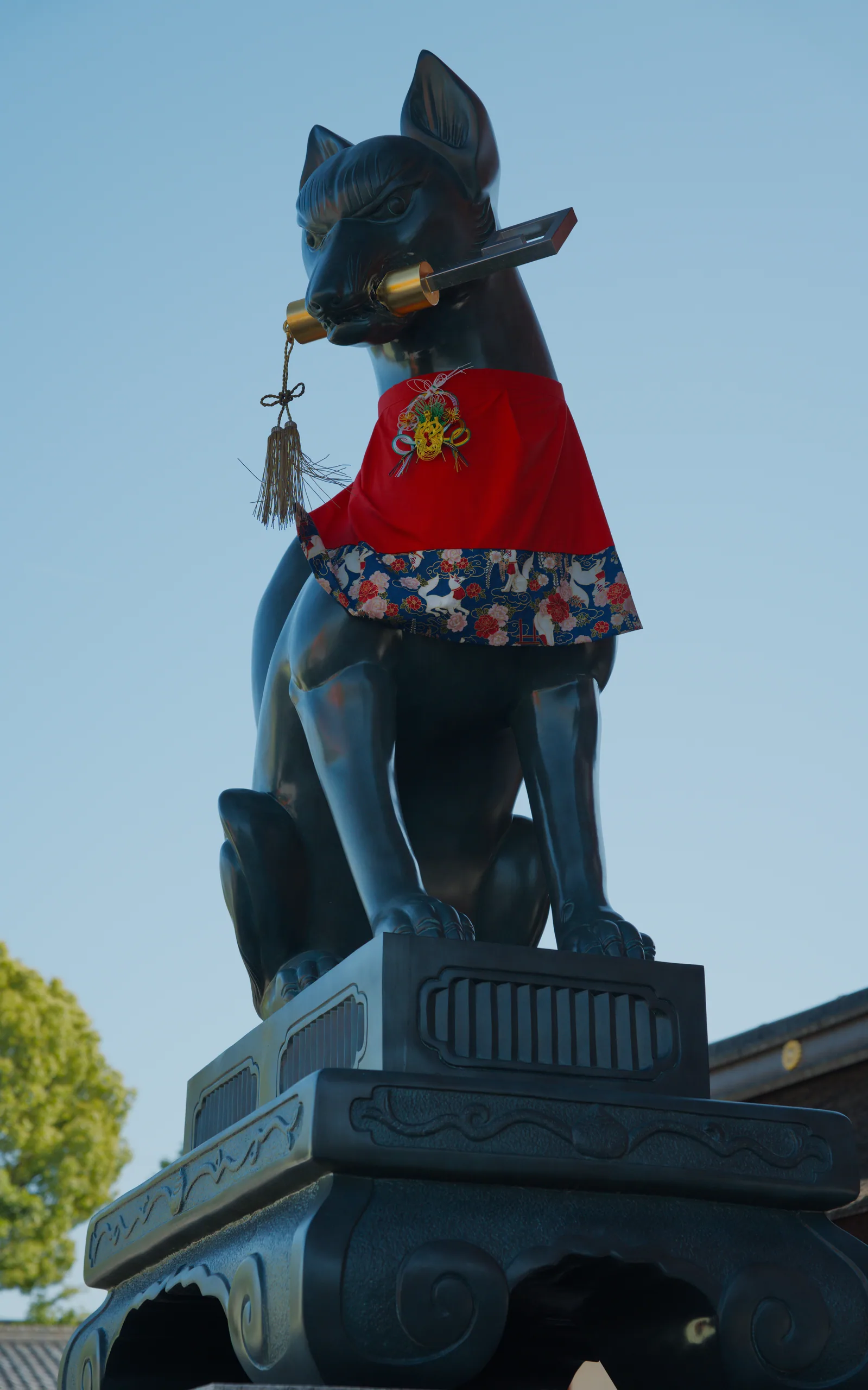 A blue fox statue wearing a red cloth draped across its back, standing on a pedestal.
