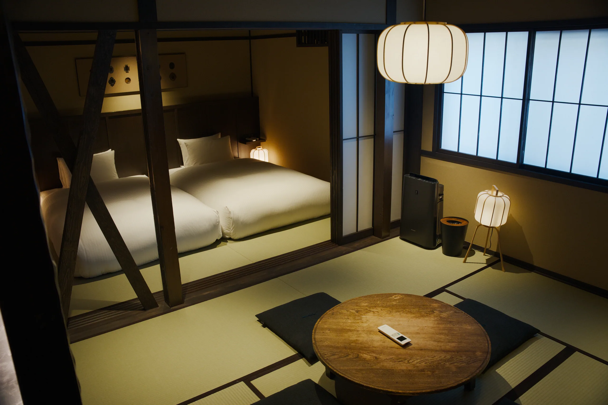A tatami room with a wooden frame, round wooden table, and paper lantern.