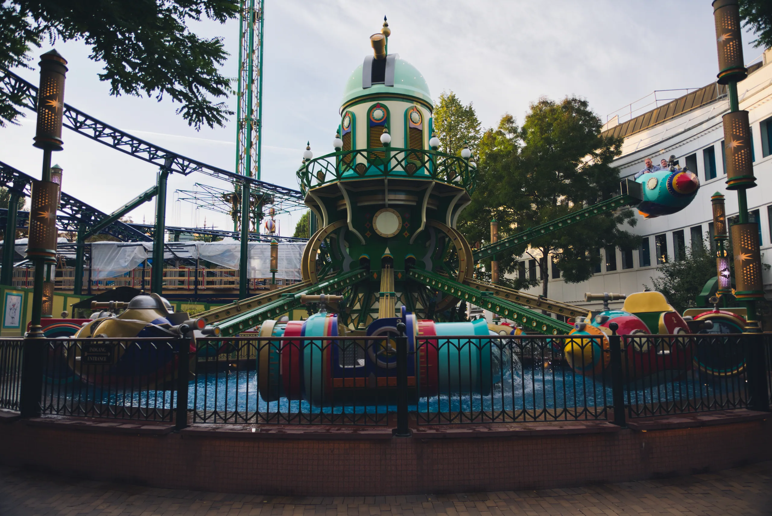 A fairground ride with a green domed tower at its centre, roller coaster track and pavilions rising behind it.