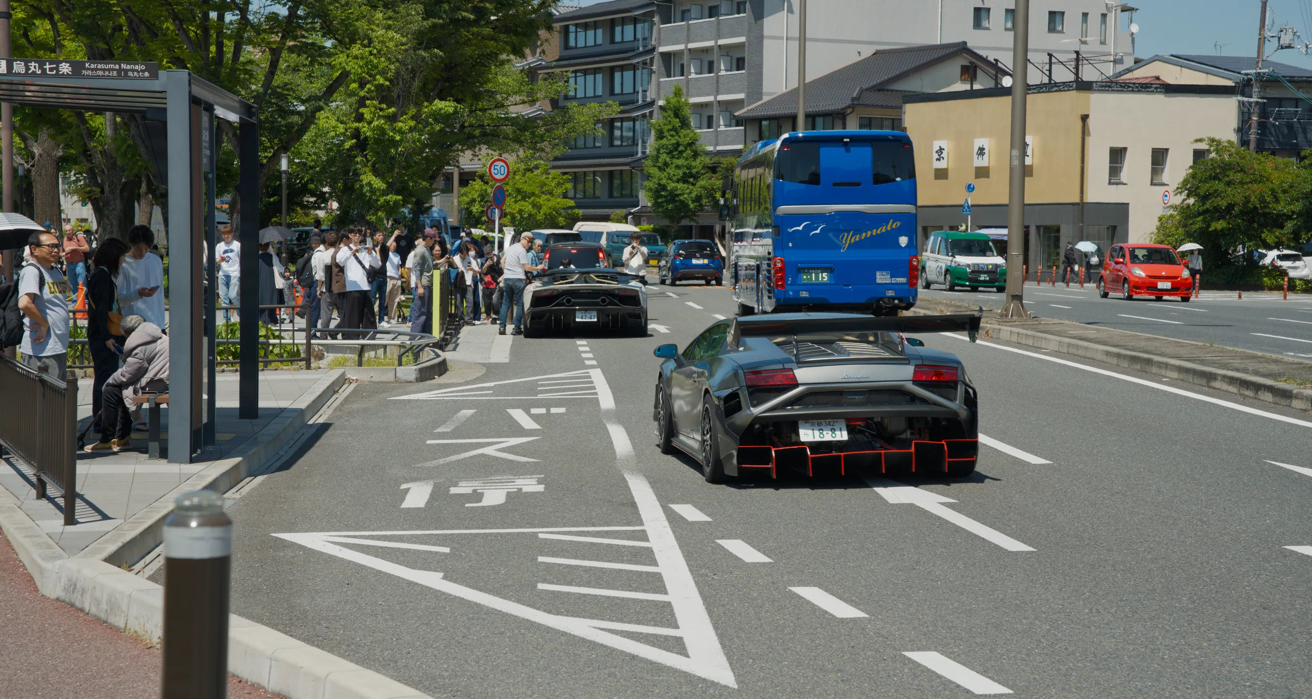 An urban street lined with buildings and vehicles under bright sunlight.