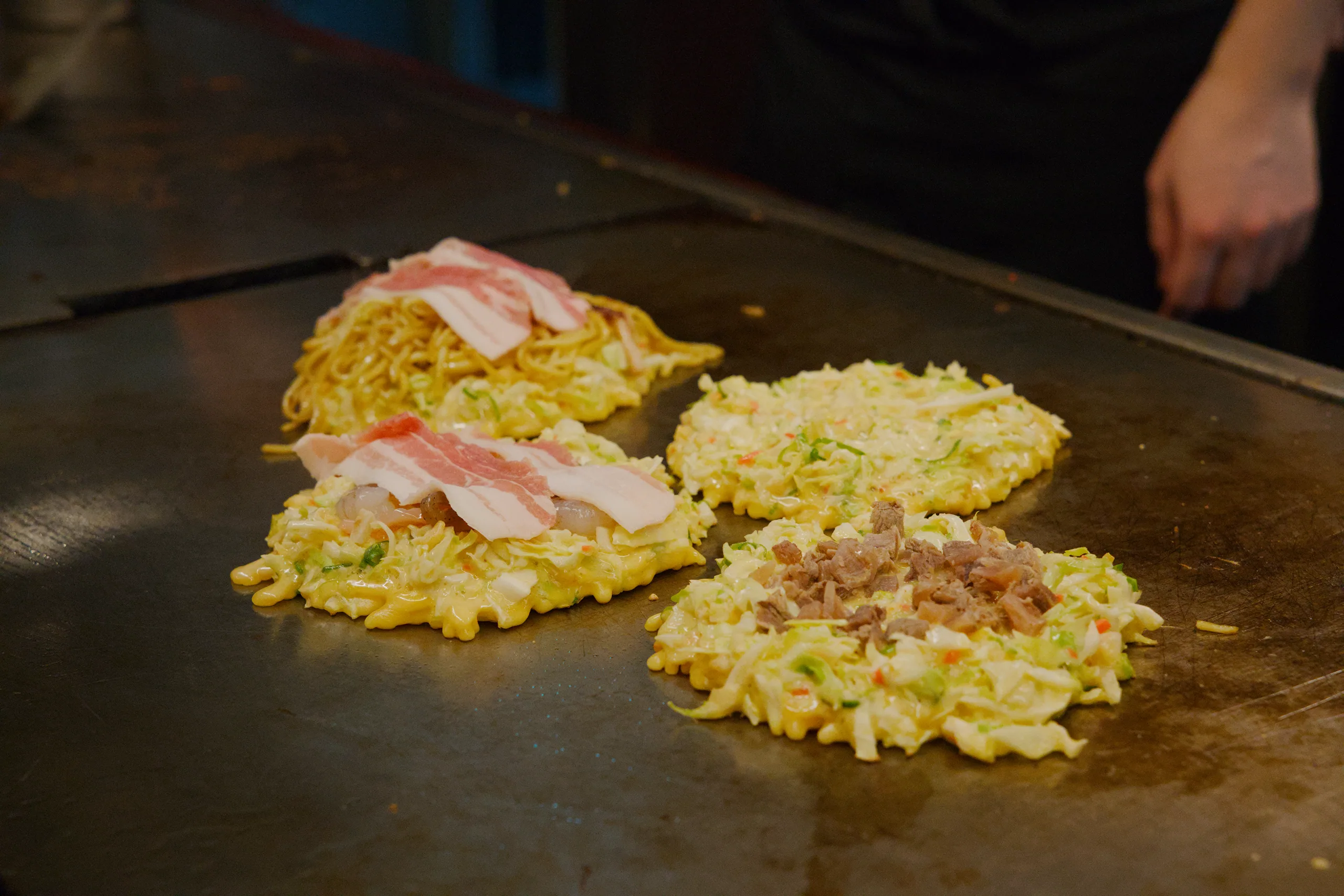 Okonomiyaki topped with pink garnish arranged on a dark surface.