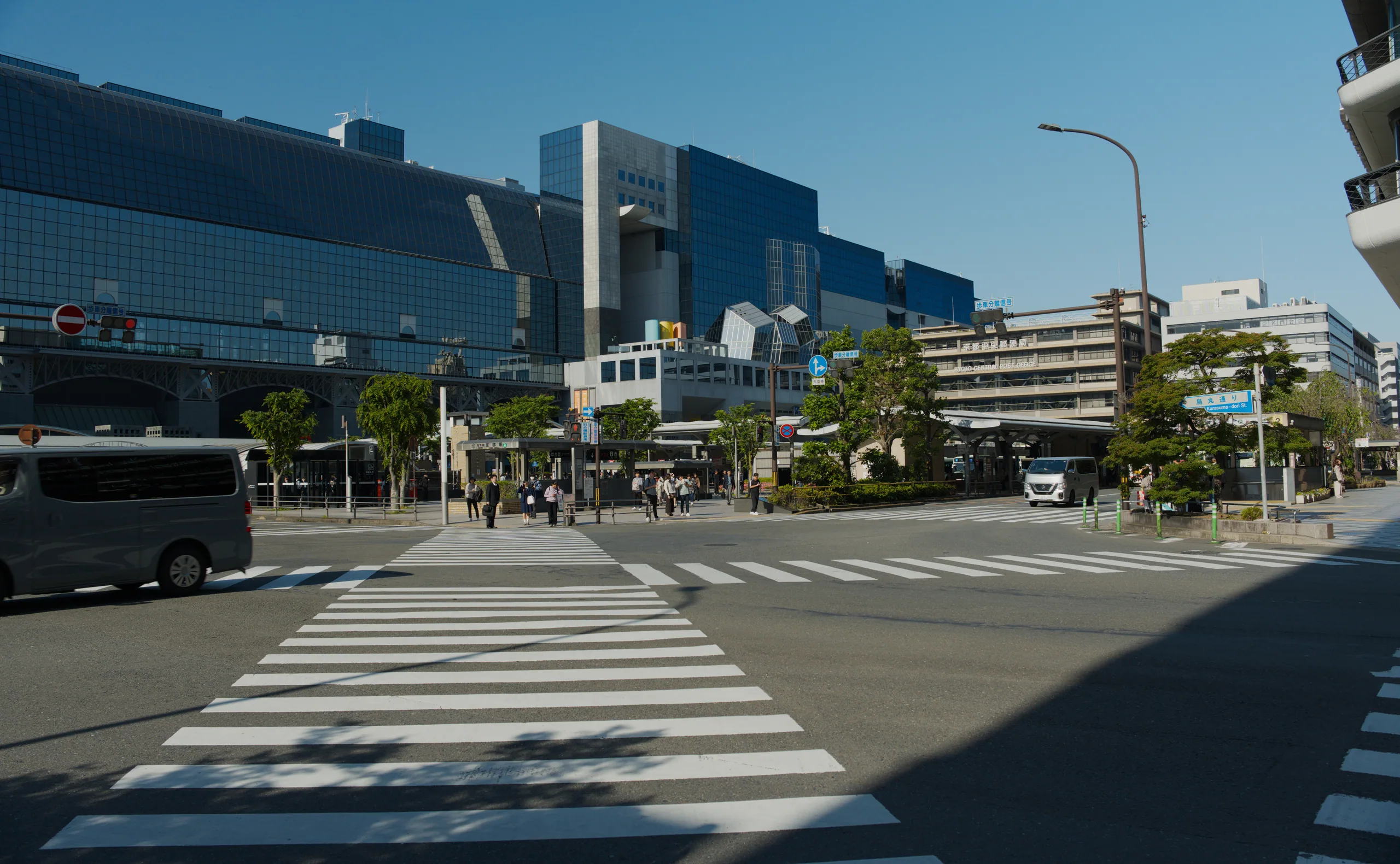 A street crossing with a red Japanese torii gate, modern buildings and people under clear sky.