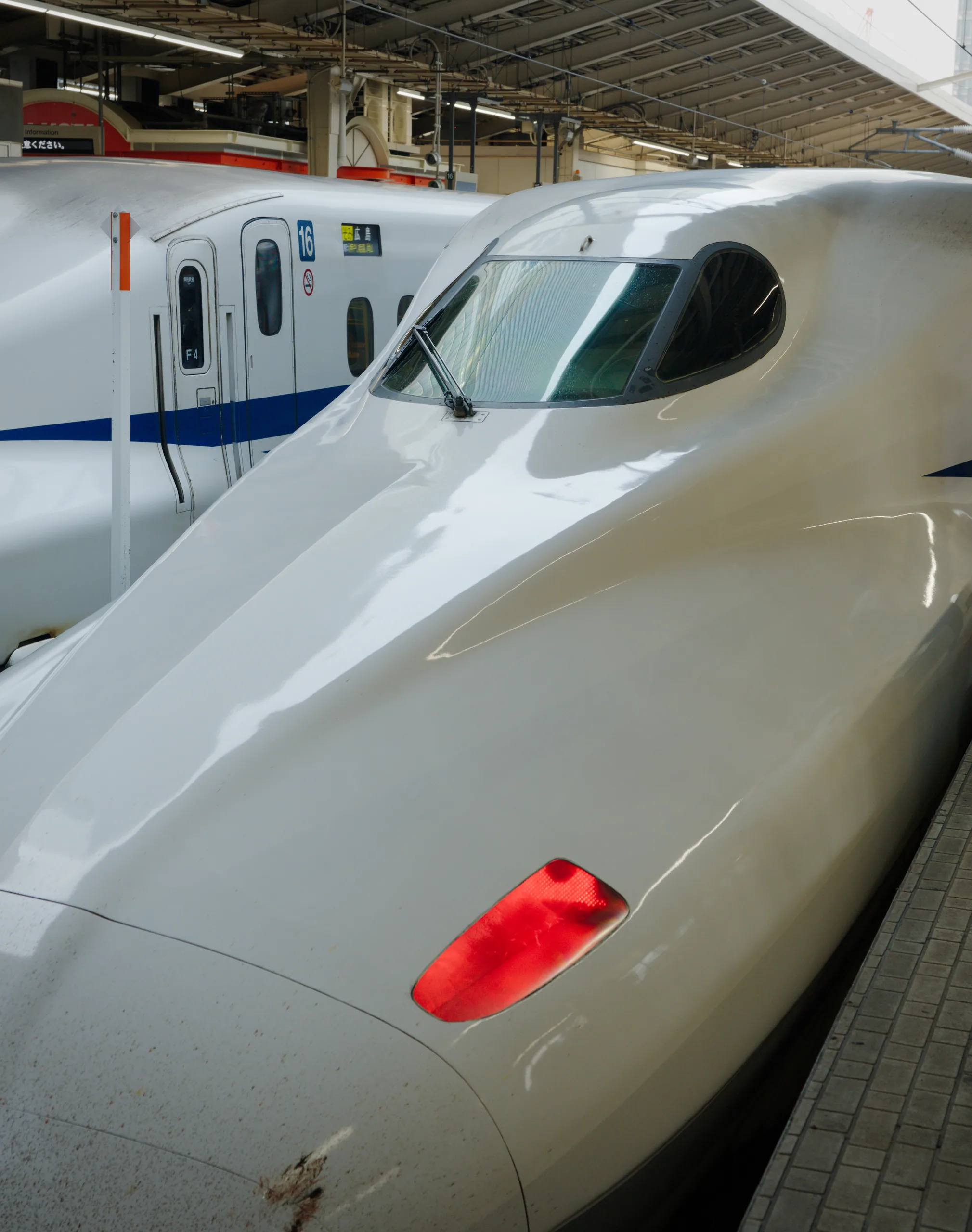 White shinkansen nose and fuselage with red taillight at a station platform.