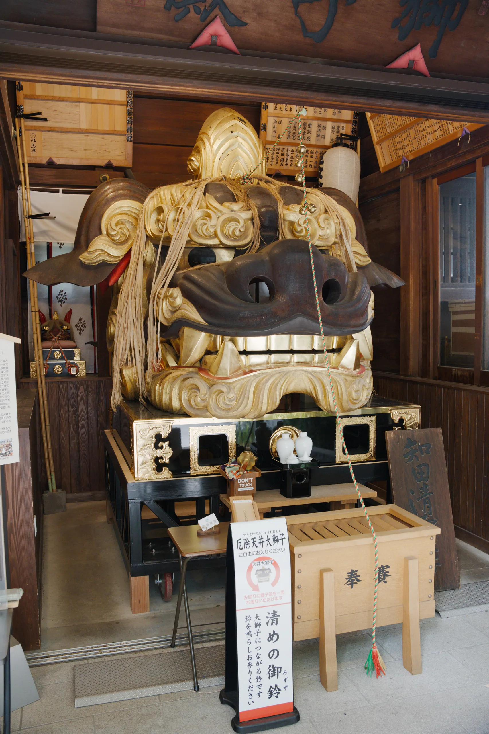 Interior of a Japanese shrine with a golden ornamental element, wooden fixtures, and shelving.