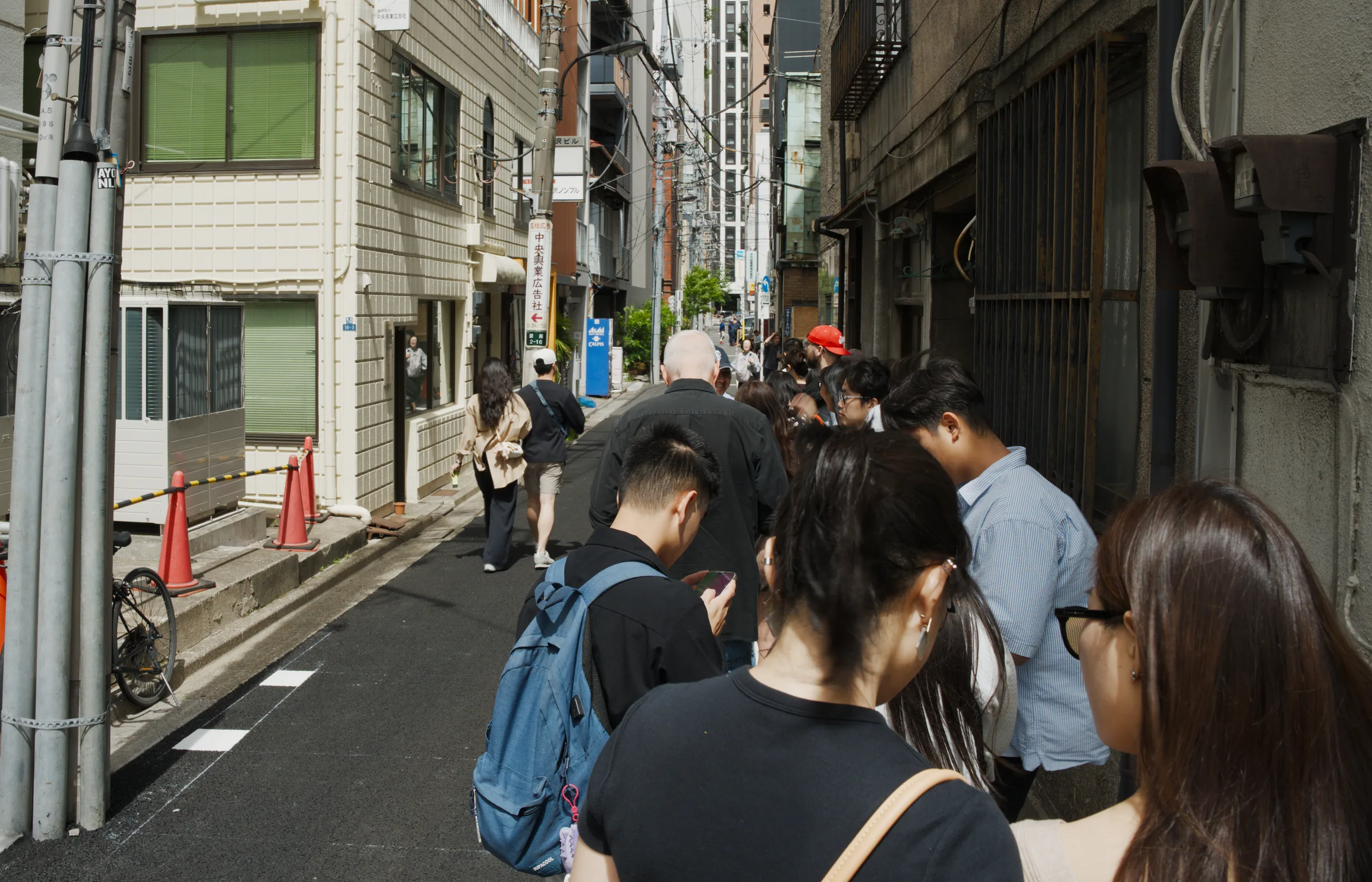 Pedestrians walking down a narrow shopping street lined with storefronts and paper lanterns.
