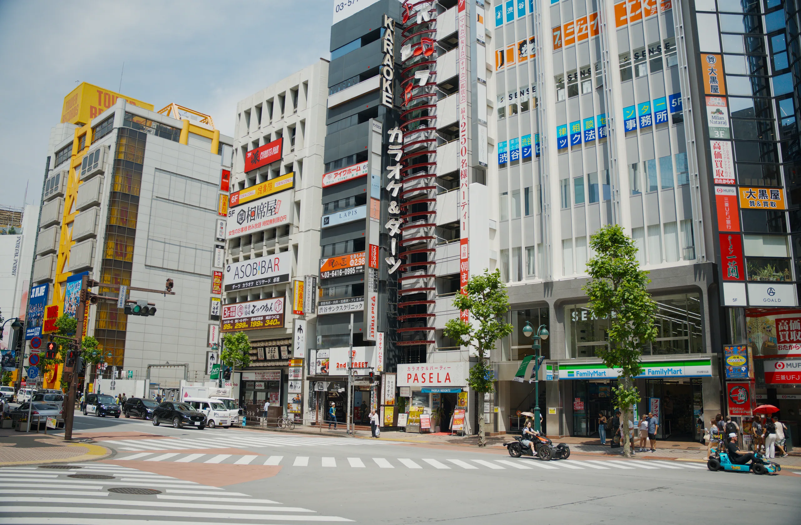 A busy shopping street lined with tall buildings and colorful storefront signs, with pedestrians crossing.