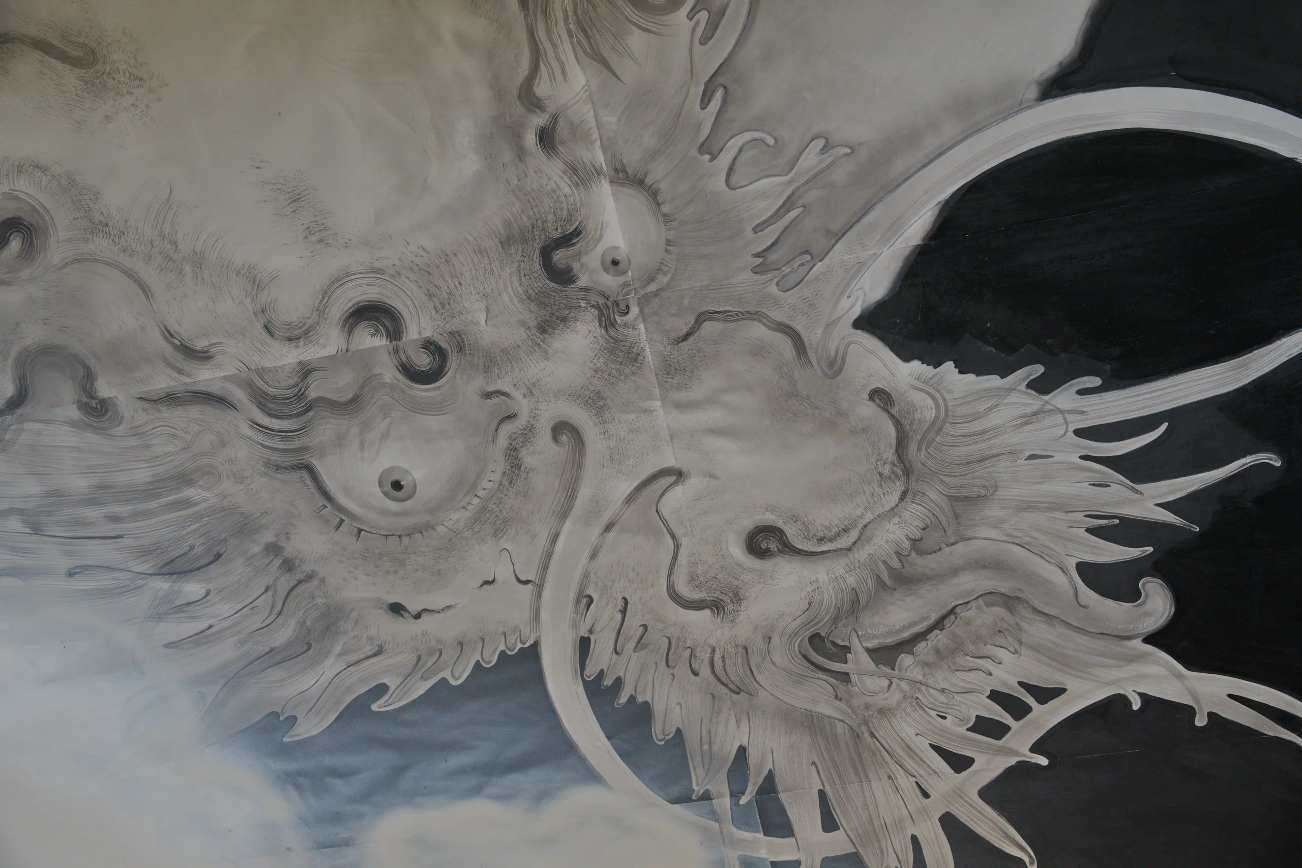 Carved white plaster relief of an ornate dragon face with detailed feathered patterns.