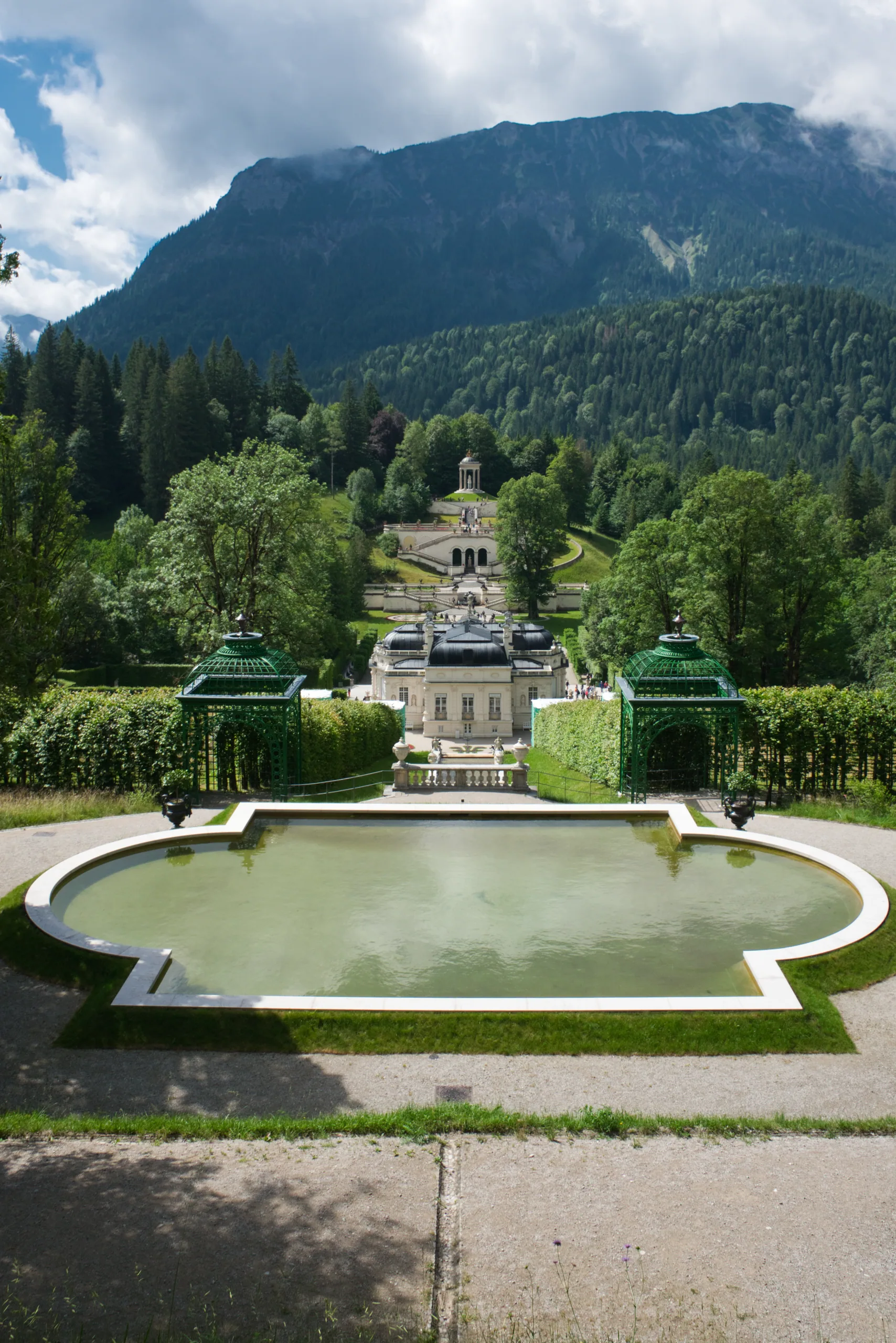 Linderhof palace across its oval basin, the wooded slope and a rocky ridge rising steeply behind.